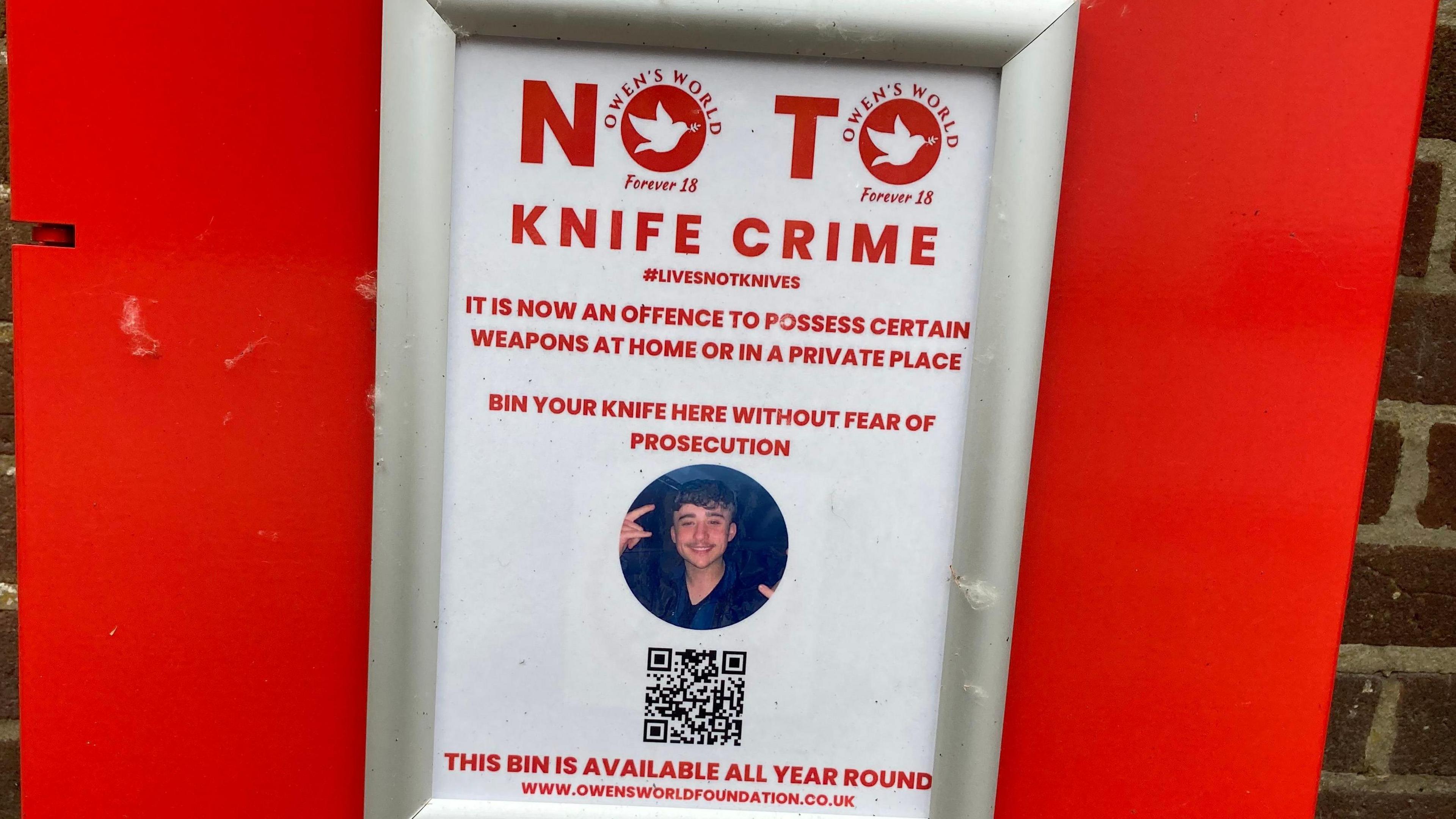 A notice attached to a bright red bin reading: "No to knife crime. It is now an offence to possess certain weapons at home or in a private place. Bin your knife here without fear of prosecution. This bin is available all year round."