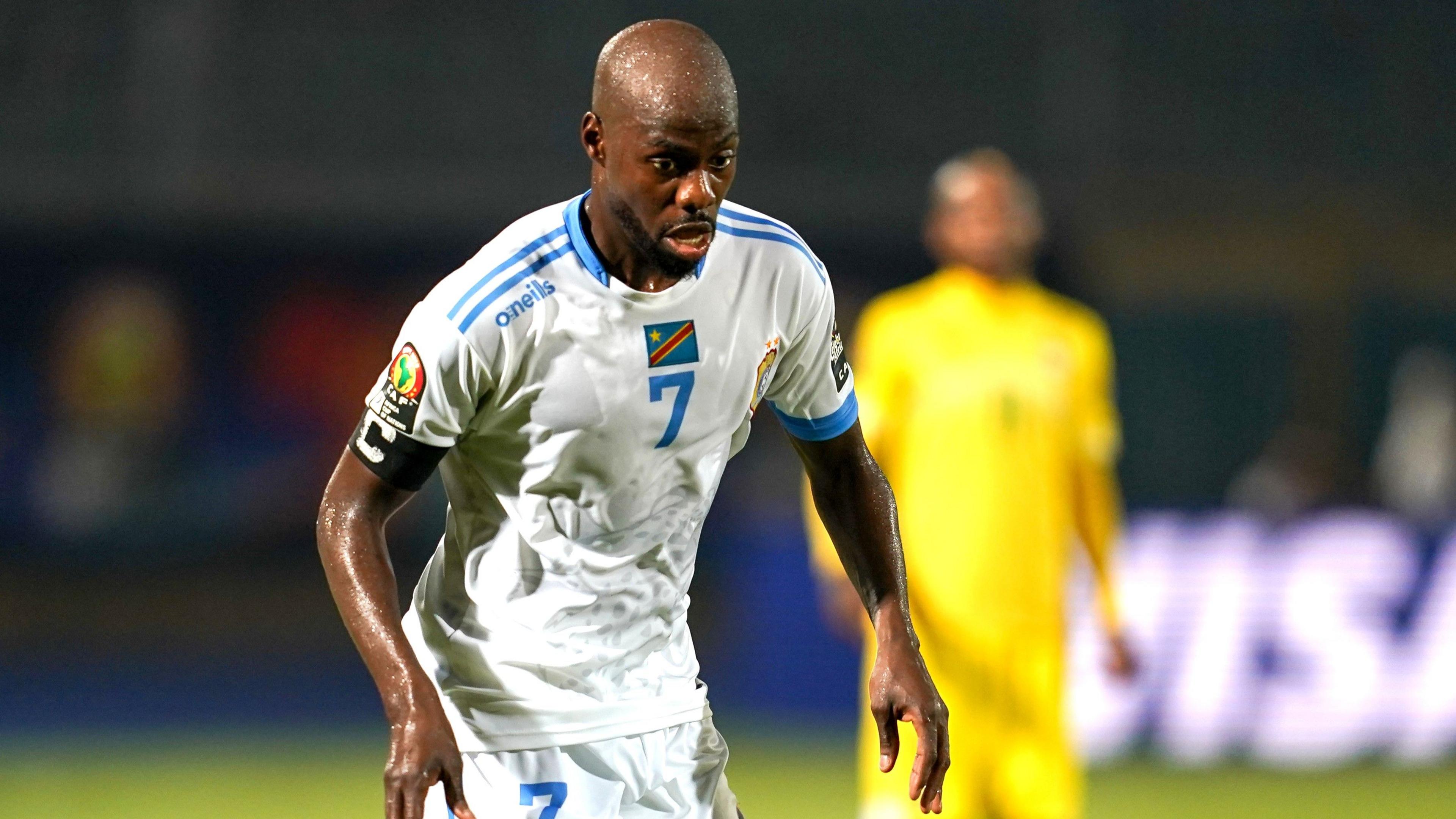 Youssouf Mulumbu wears a white football shirt with blue trim which bears a DR Congo flag and the number seven on the front