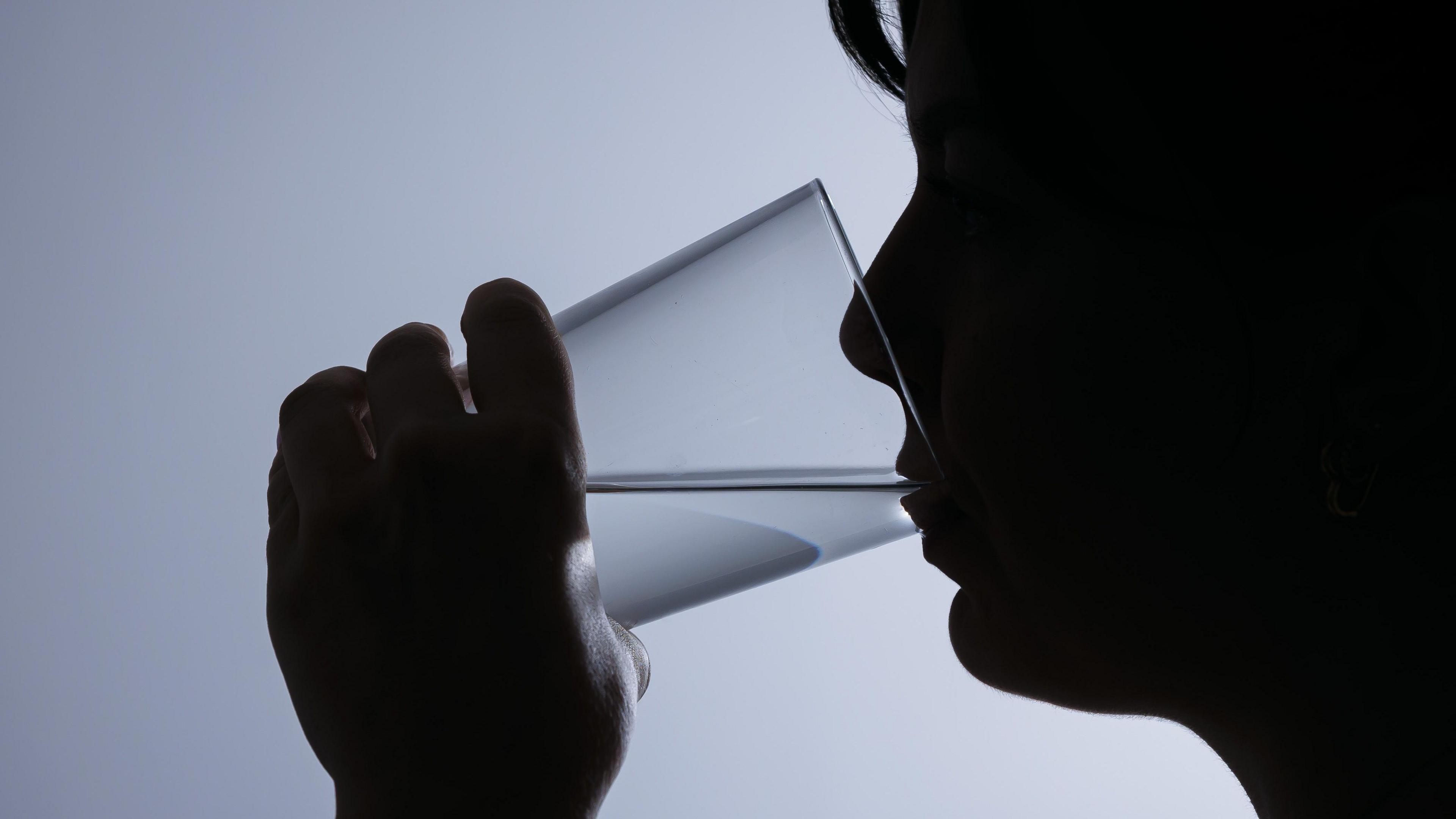 The silhouette of a woman drinking from a glass which has water in it.