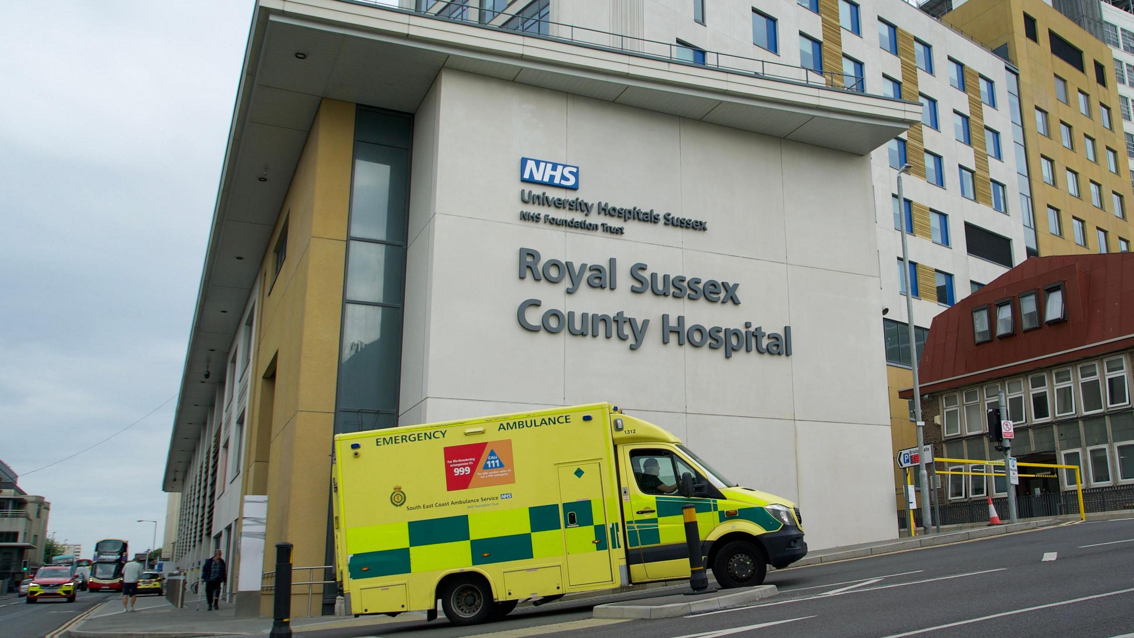 A bright yellow and green ambulance outside a modern hospital building. 