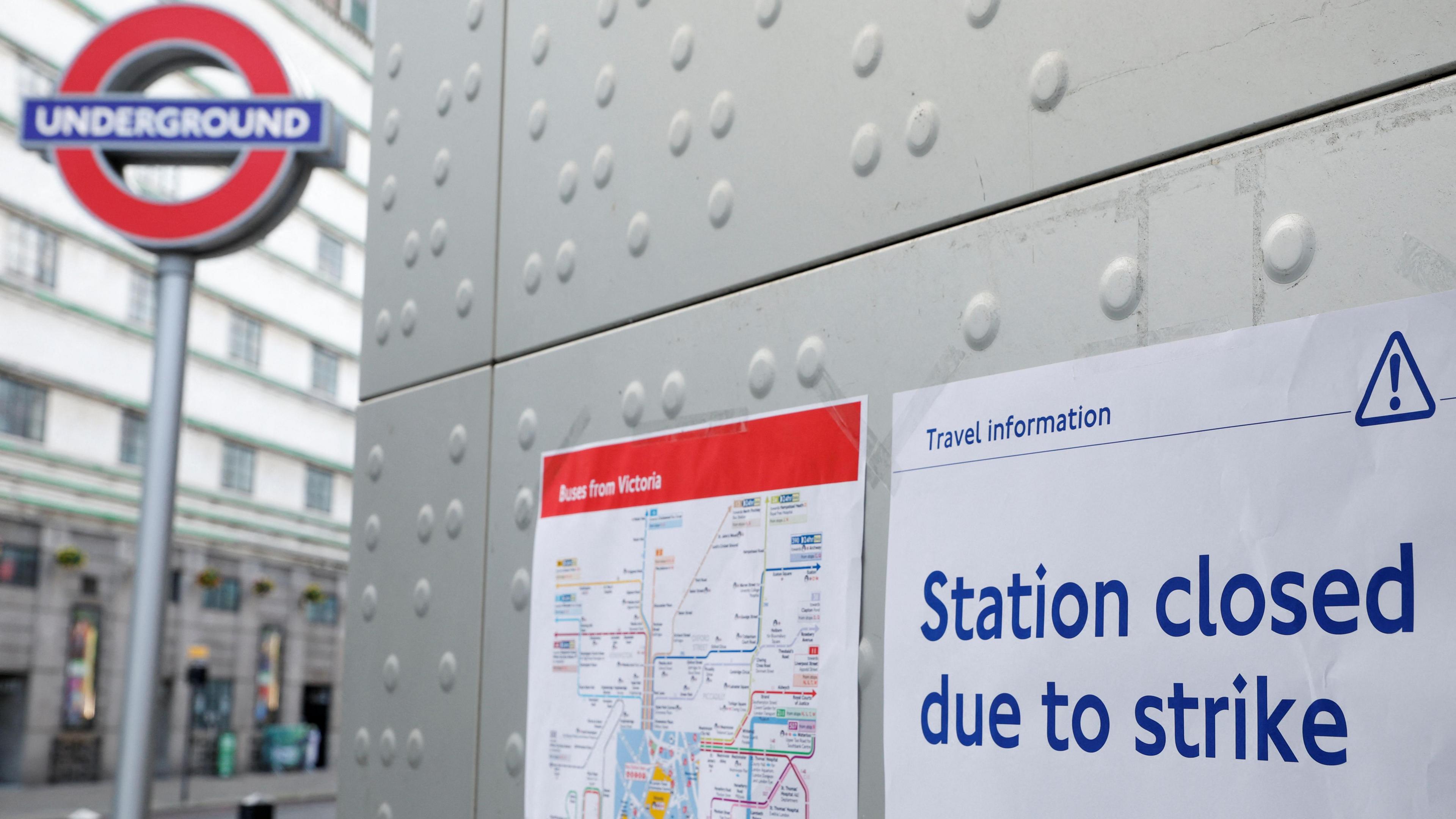 Sign on station wall reads: "Station closed due to strike". It is next to a bus route map and a tall Underground roundel sits in the background.