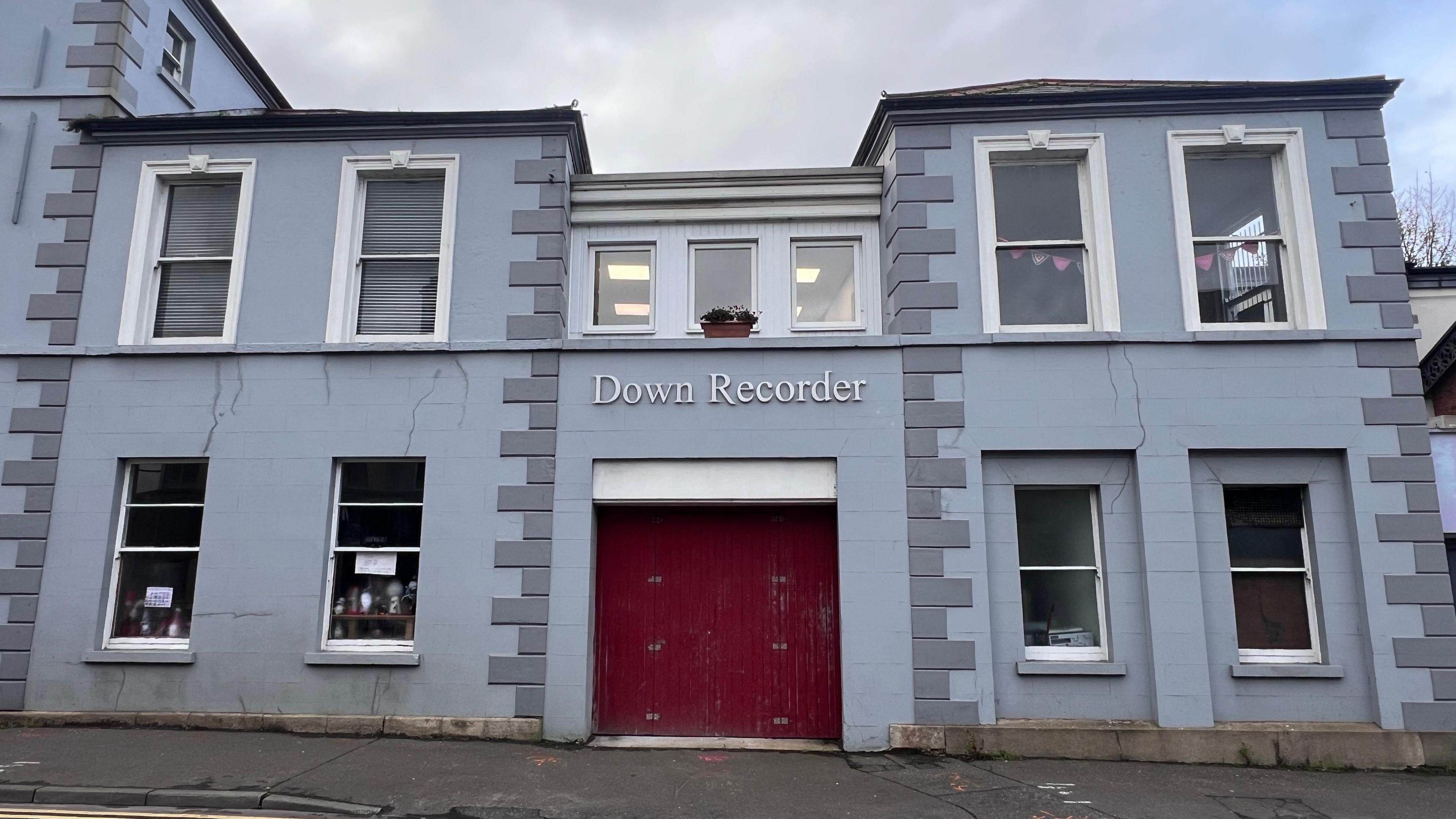 A grey building with a red door.