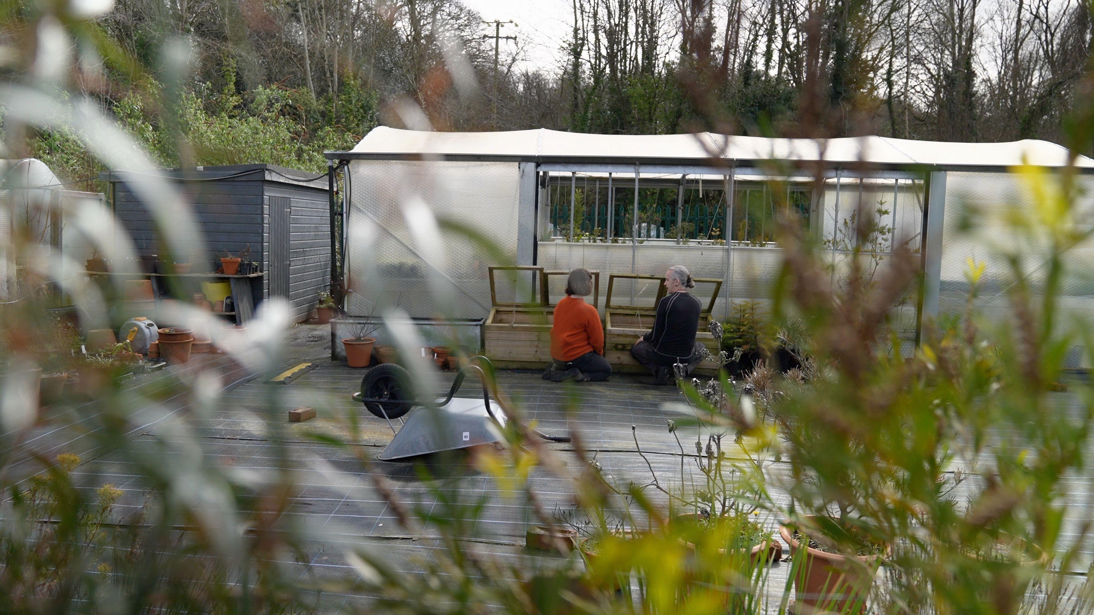 Photograph of a greenhouse with two people kneeling in front of it