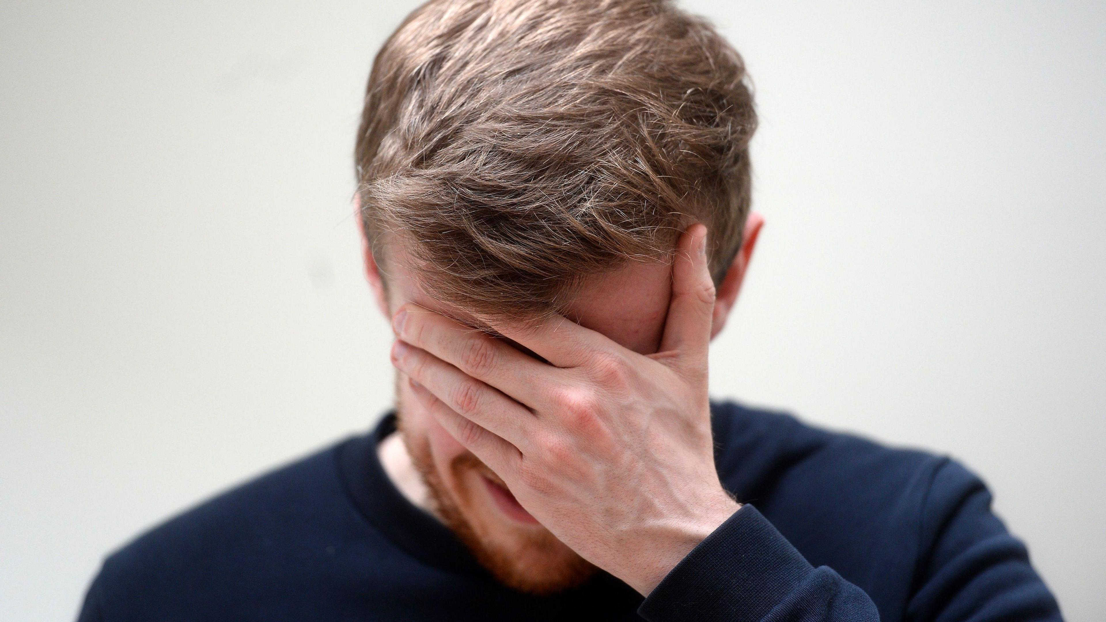 Man with brown hair holding his hand to his face in anguish