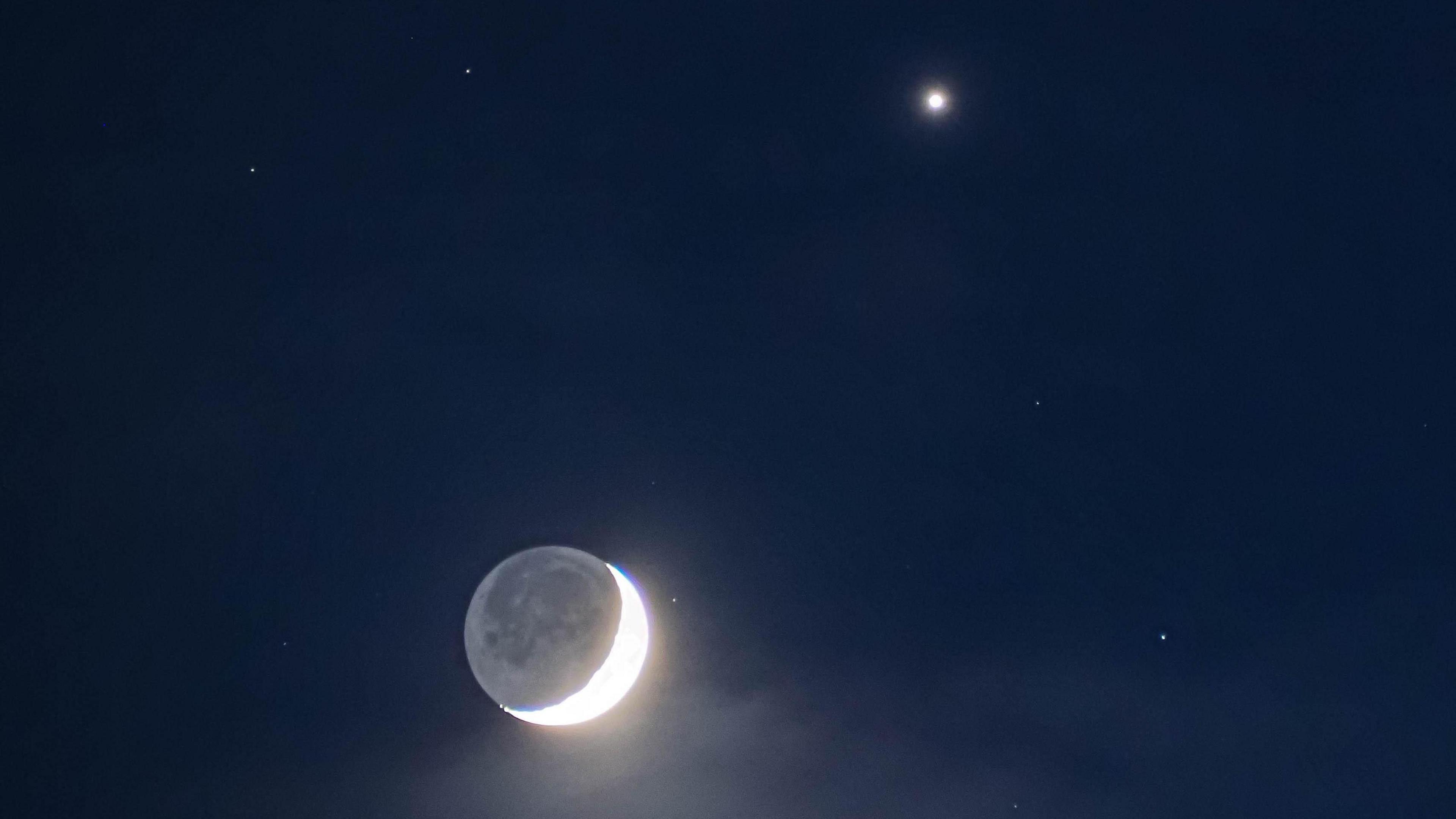 A crescent moon and Venus against a dark sky.