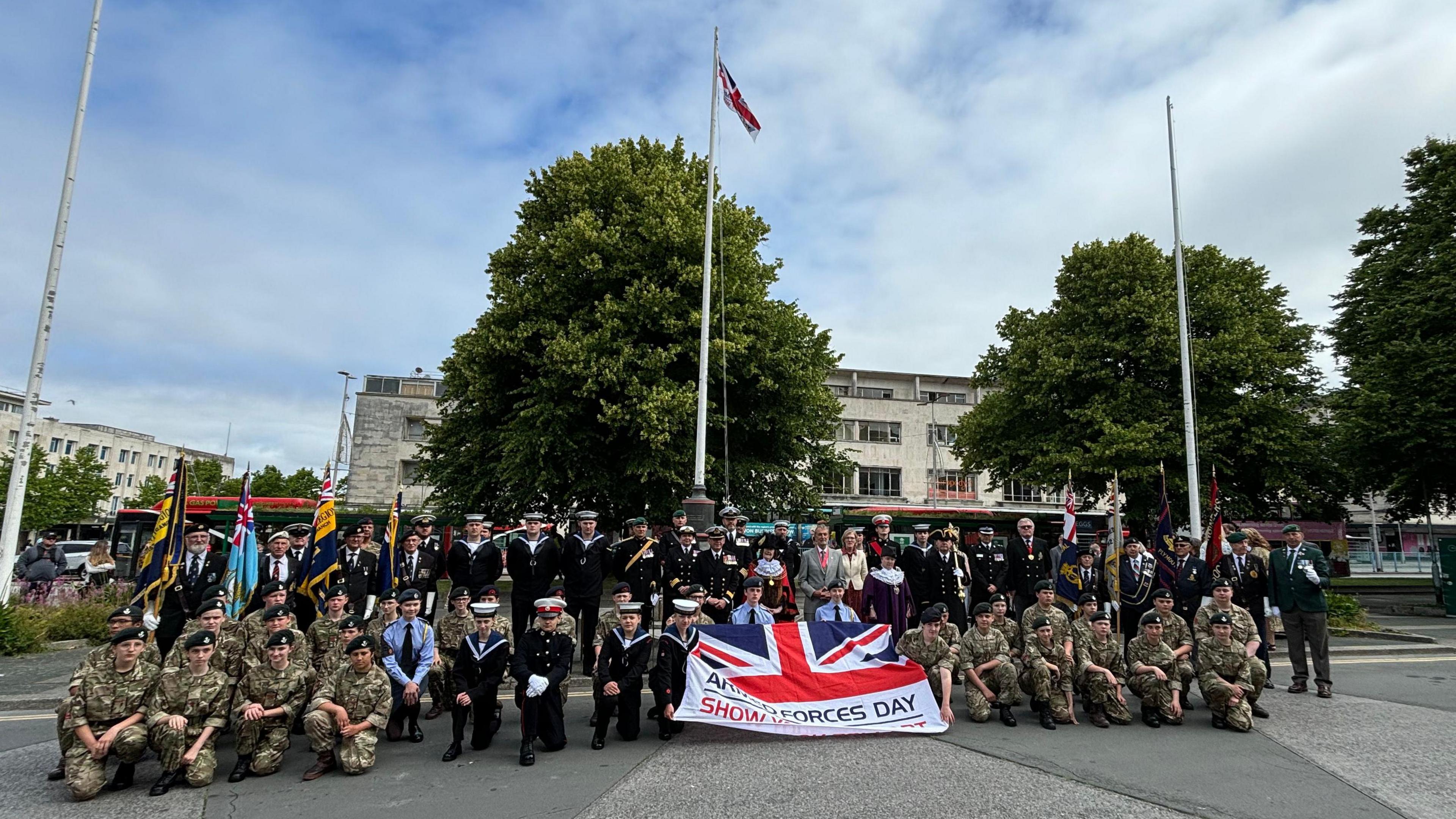 A large group of military personnel in uniform holding a Union Jack flag in Plymouth City Centre.