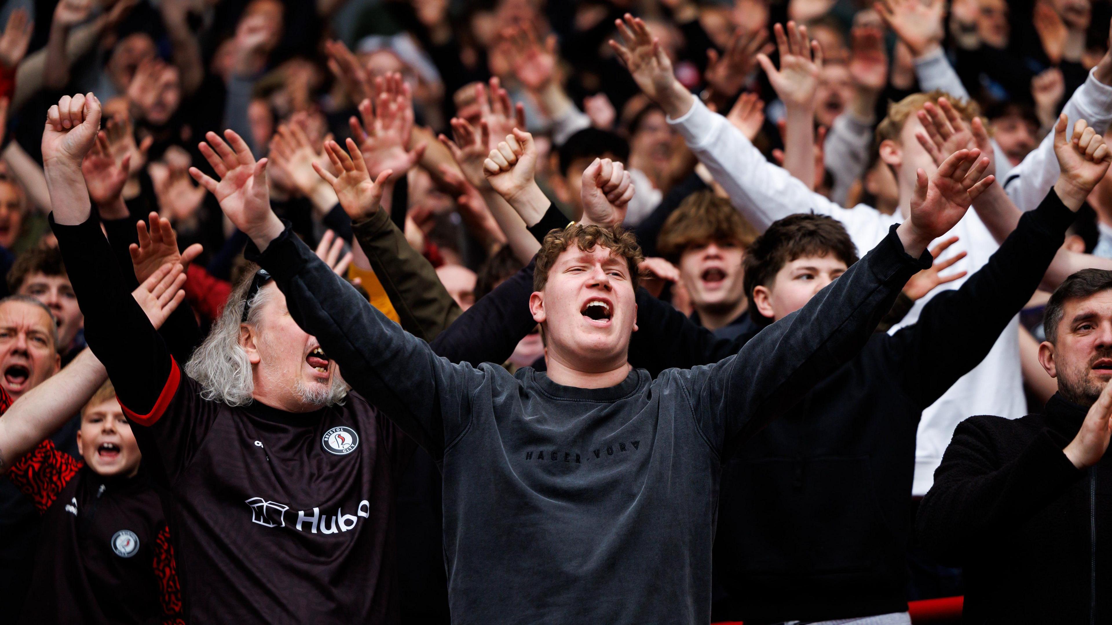 Bristol City fans in the stands sing in support of their team in the match against Hull City at Ashton Gate. Many of them have their arms outstretched as they sing