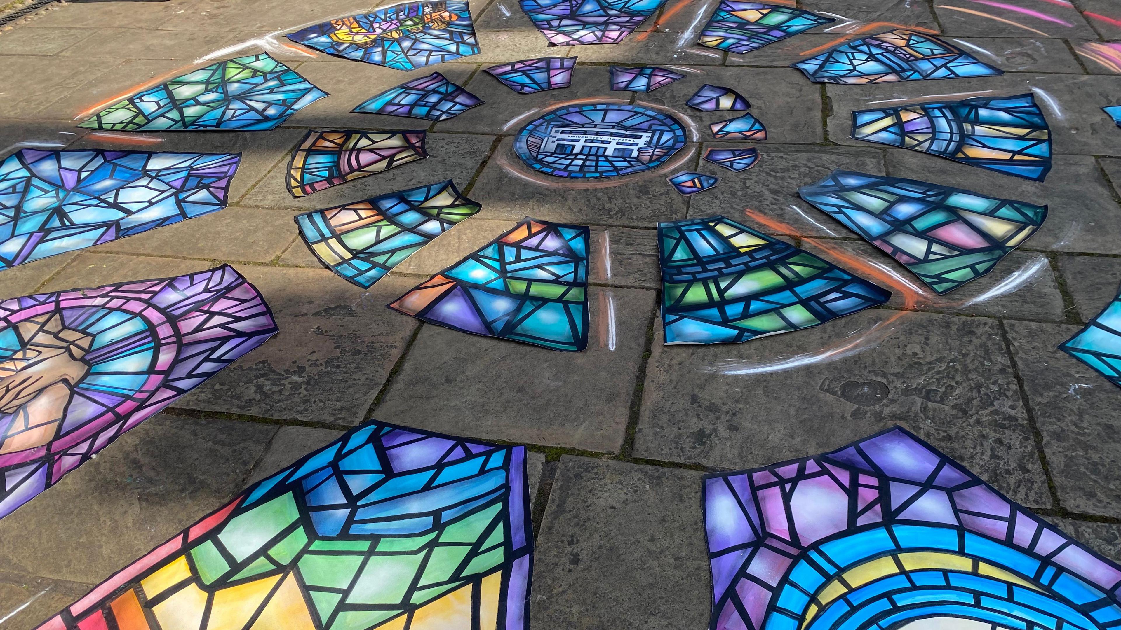 A colourful, spiralling artwork resembling a stained glass window has been created on paving slabs on the ground.