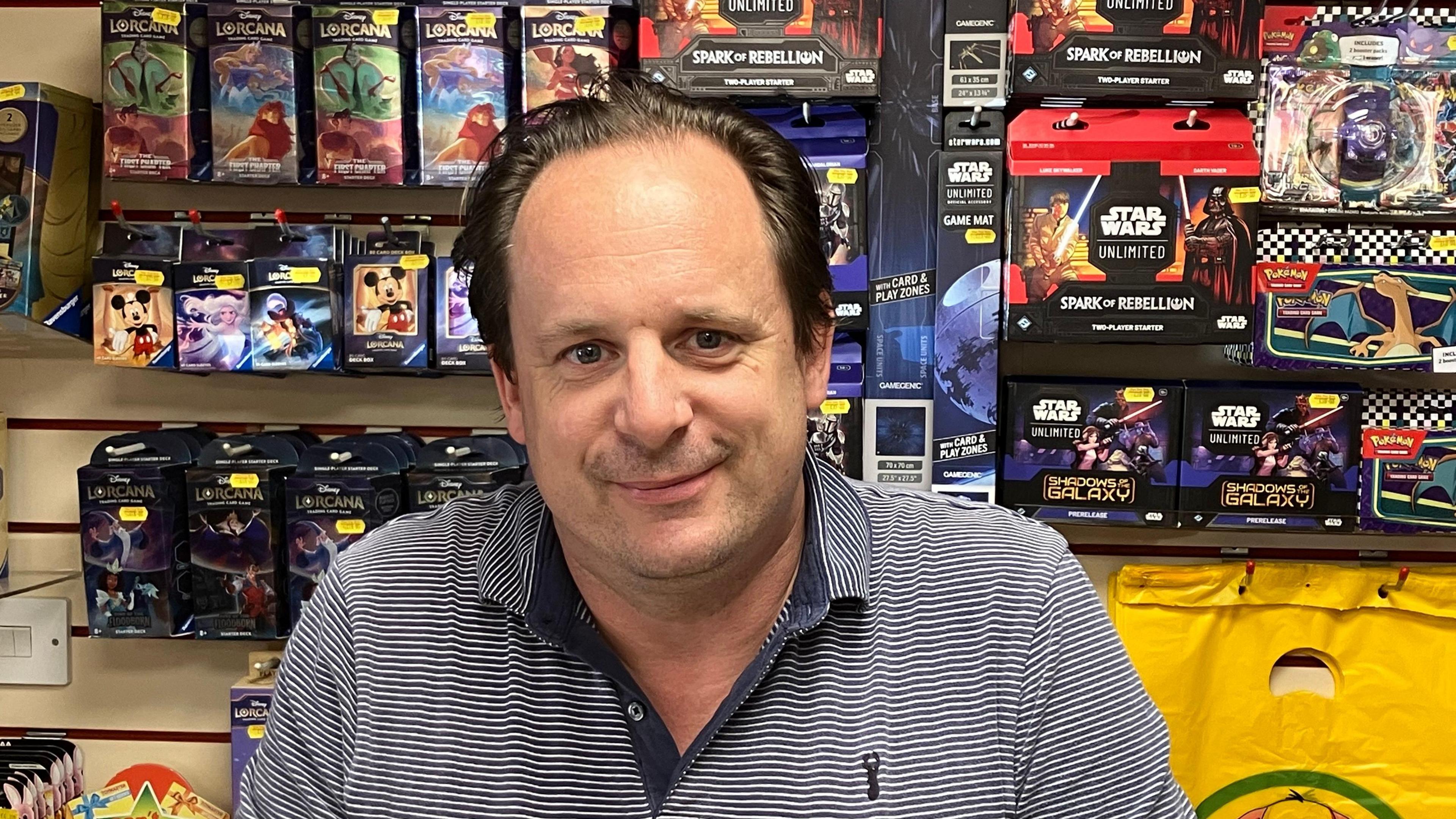 Manager of toy shop wearing striped blue top standing in front of a selection of games and toys 