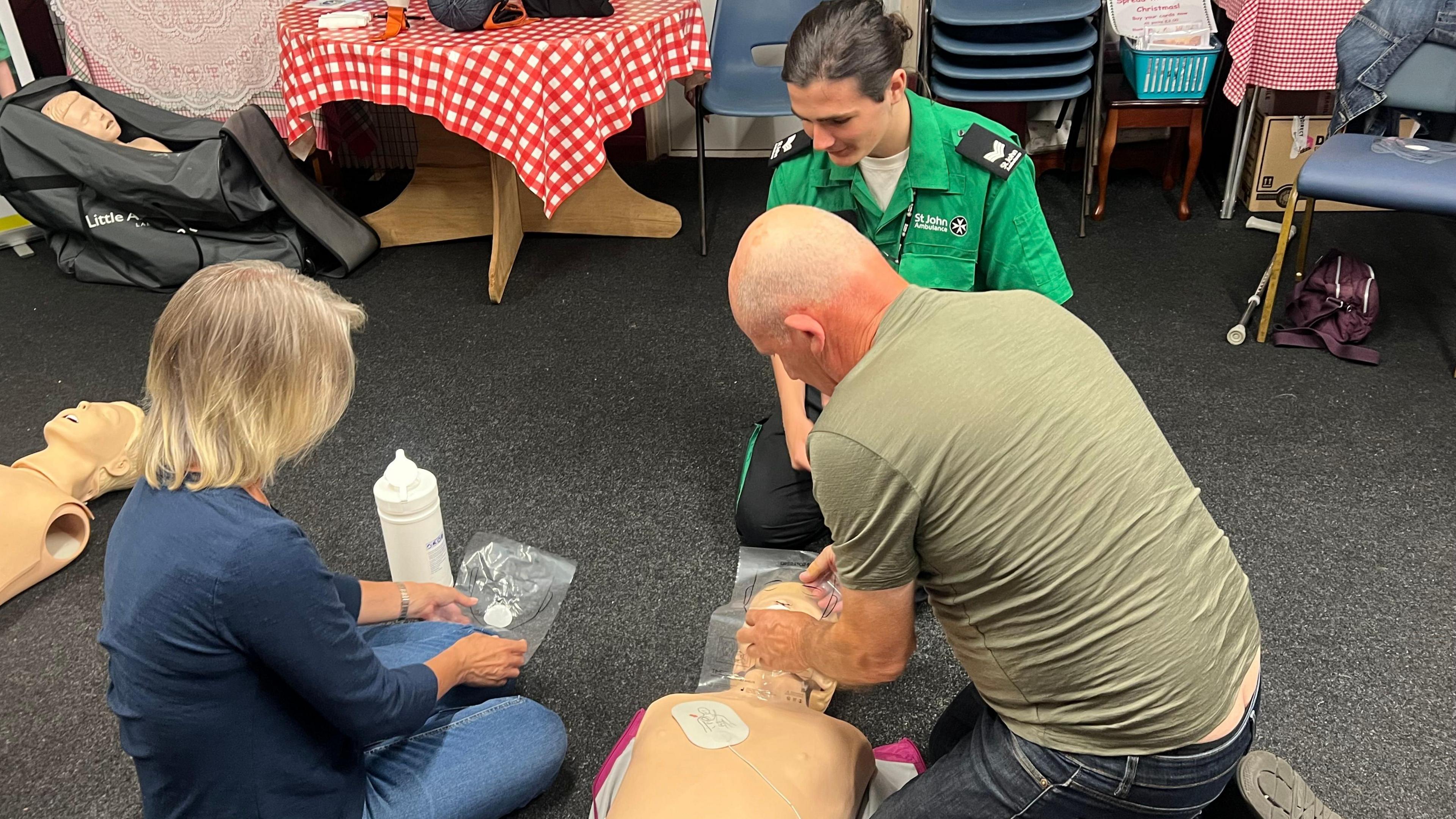 St John Ambulance volunteer watches on as a man and woman learn first aid using a mannequin.
