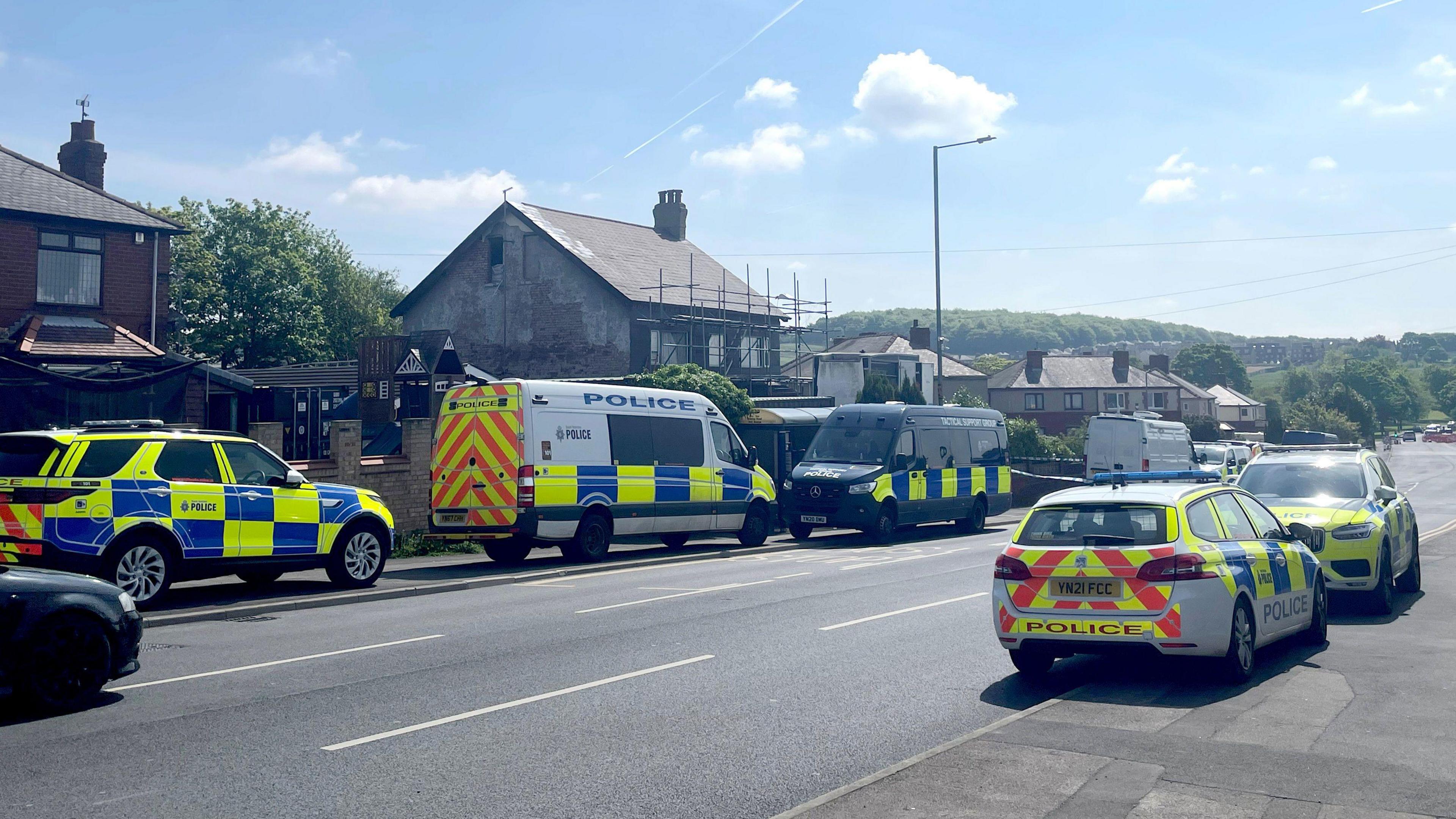 Police cars outside a house. The house has scaffolding, with the weather bright and clear.