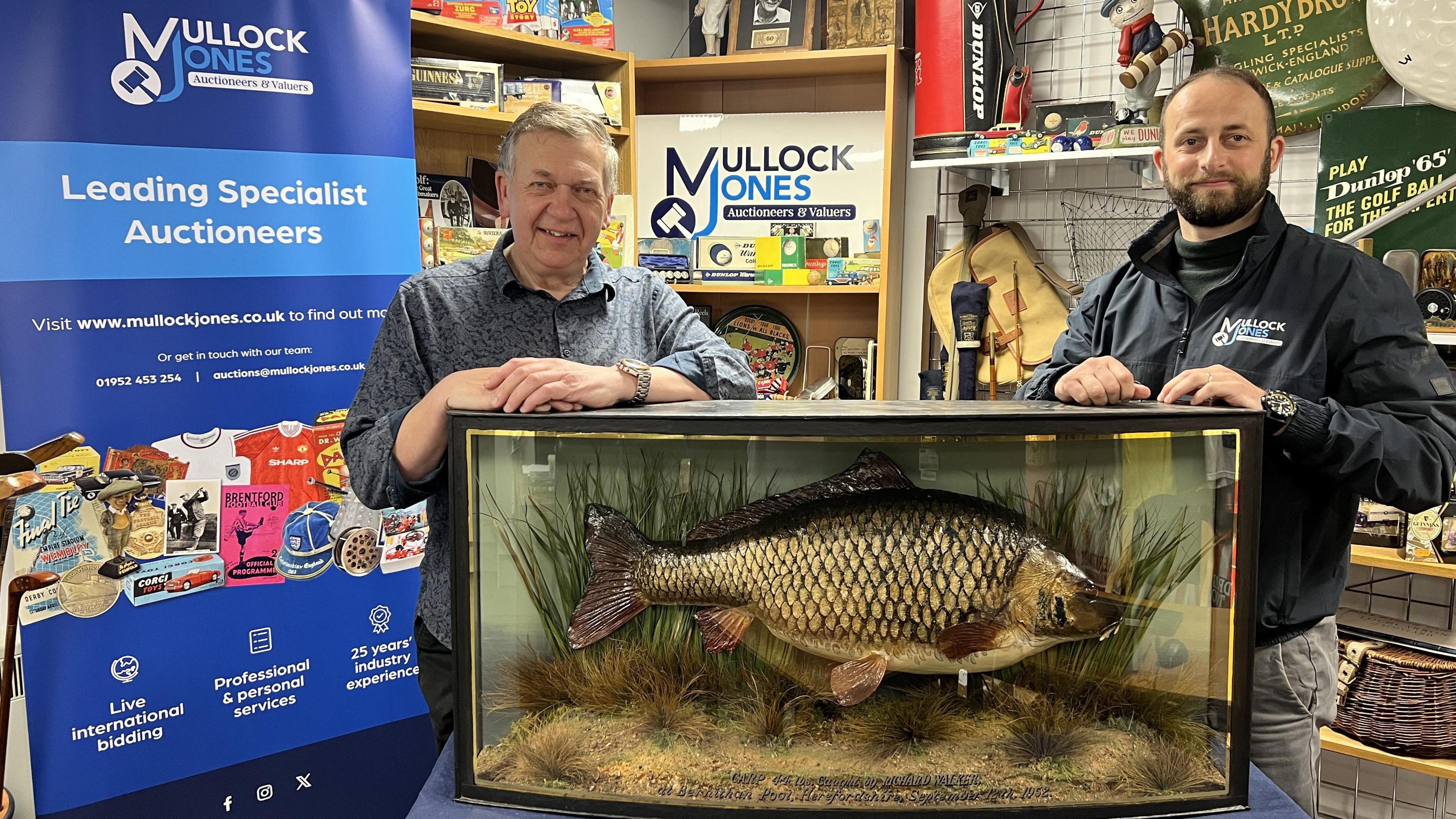 Two men standing in front of a large preserved fish in a glass case