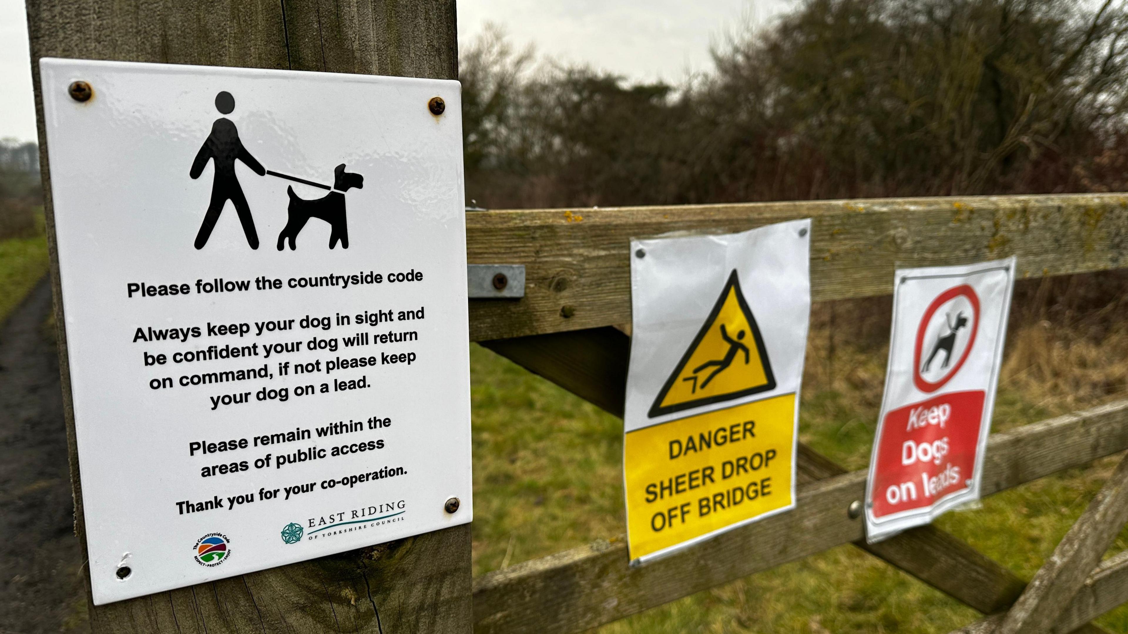 Official council Countryside Code sign advising people to keep dogs on leads. Two unofficial signs have been tacked to a gate next to the council signs - one says steep drop ahead, the other says keep dogs on leads.