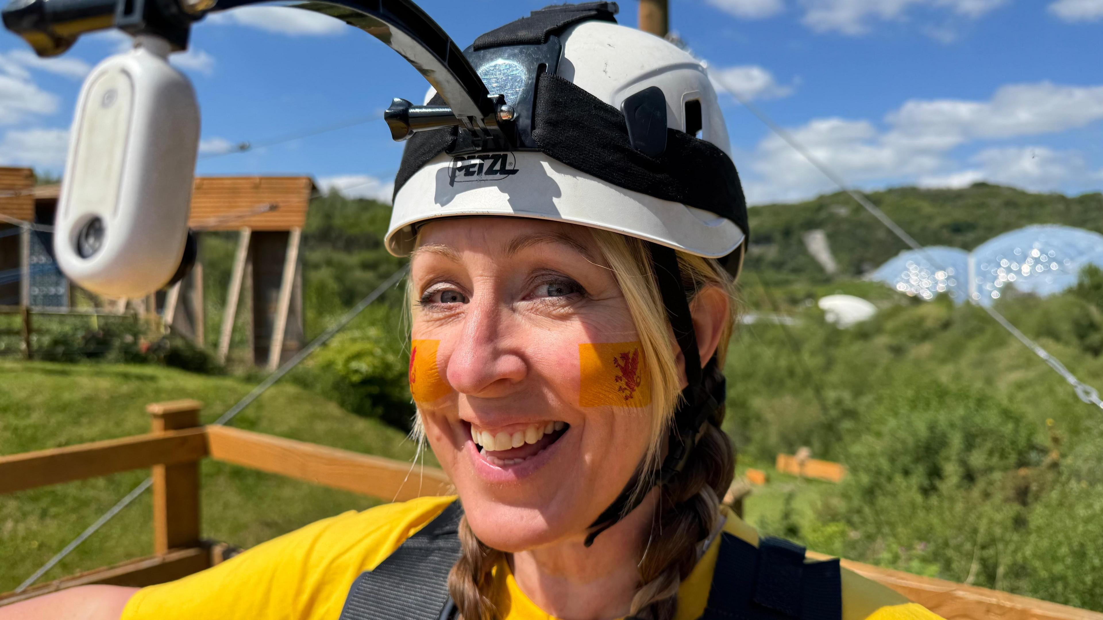 A woman is smiling at the camera. She is wearing a white helmet and has two Somerset flags painted on her face.