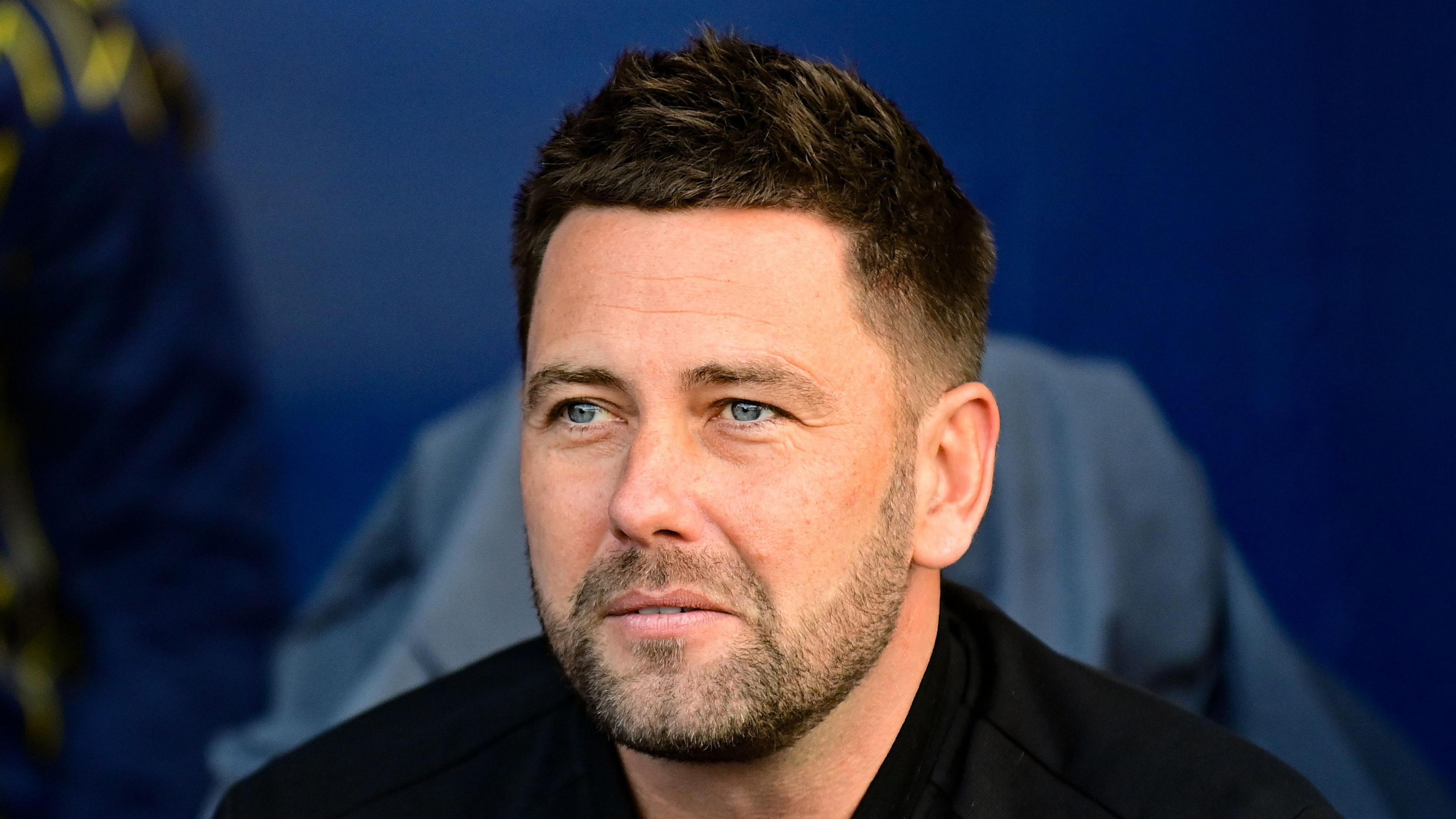 Oxford United head coach Des Buckingham sitting in the dugout during a Championship game against Stoke City