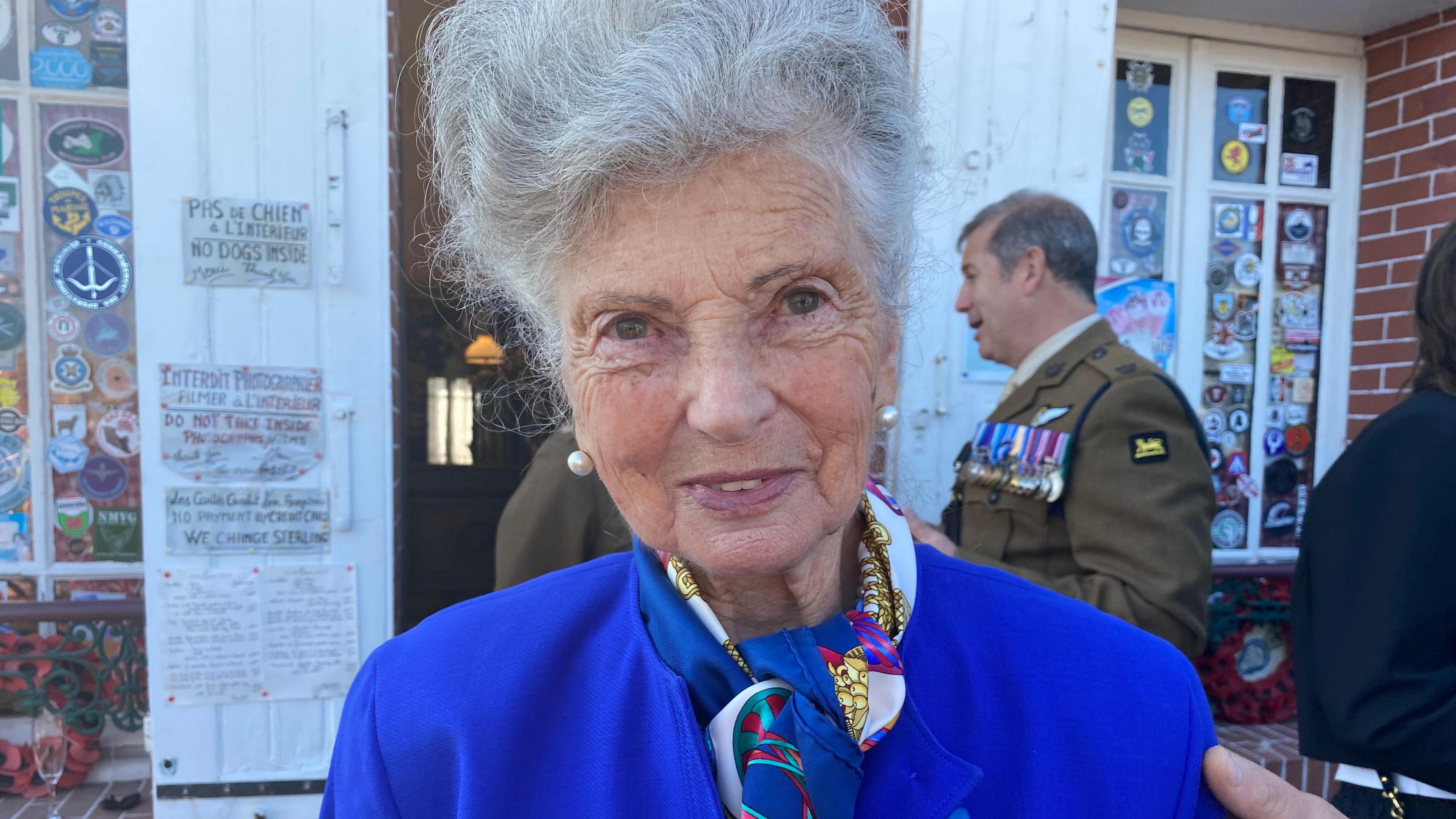 Arlette Gondree outside a café wearing a blue suit and wearing pearl earrings