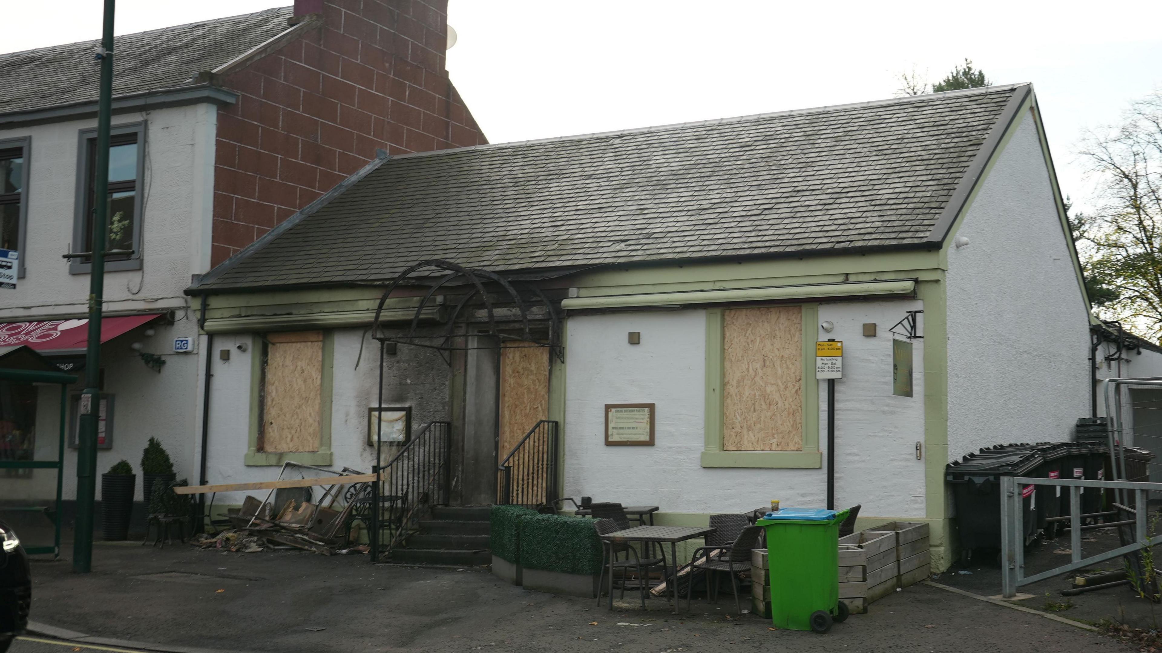 A fire damaged restaurant building, with boarded up windows and charred damaged around it