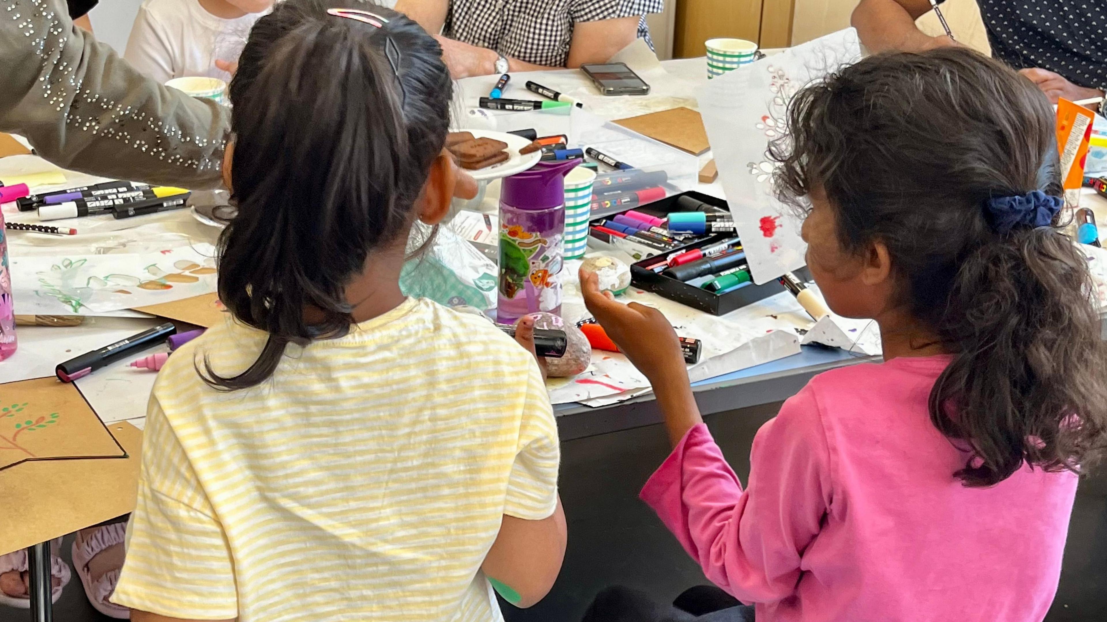 The back view of two young children in front of a table covered in art equipment