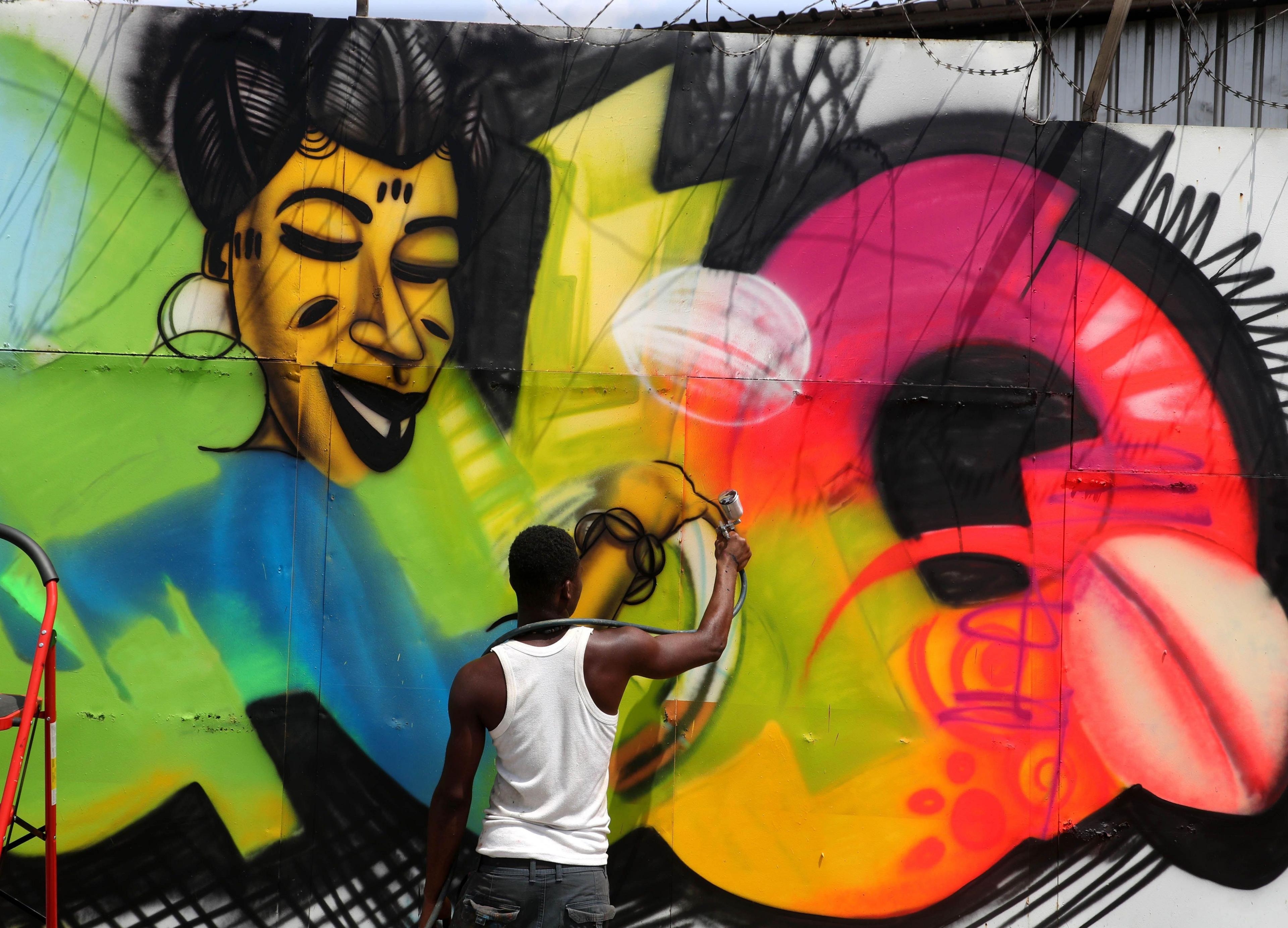 A man spray-paints a mural in bright colours on a large concrete wall in Abidjan.
