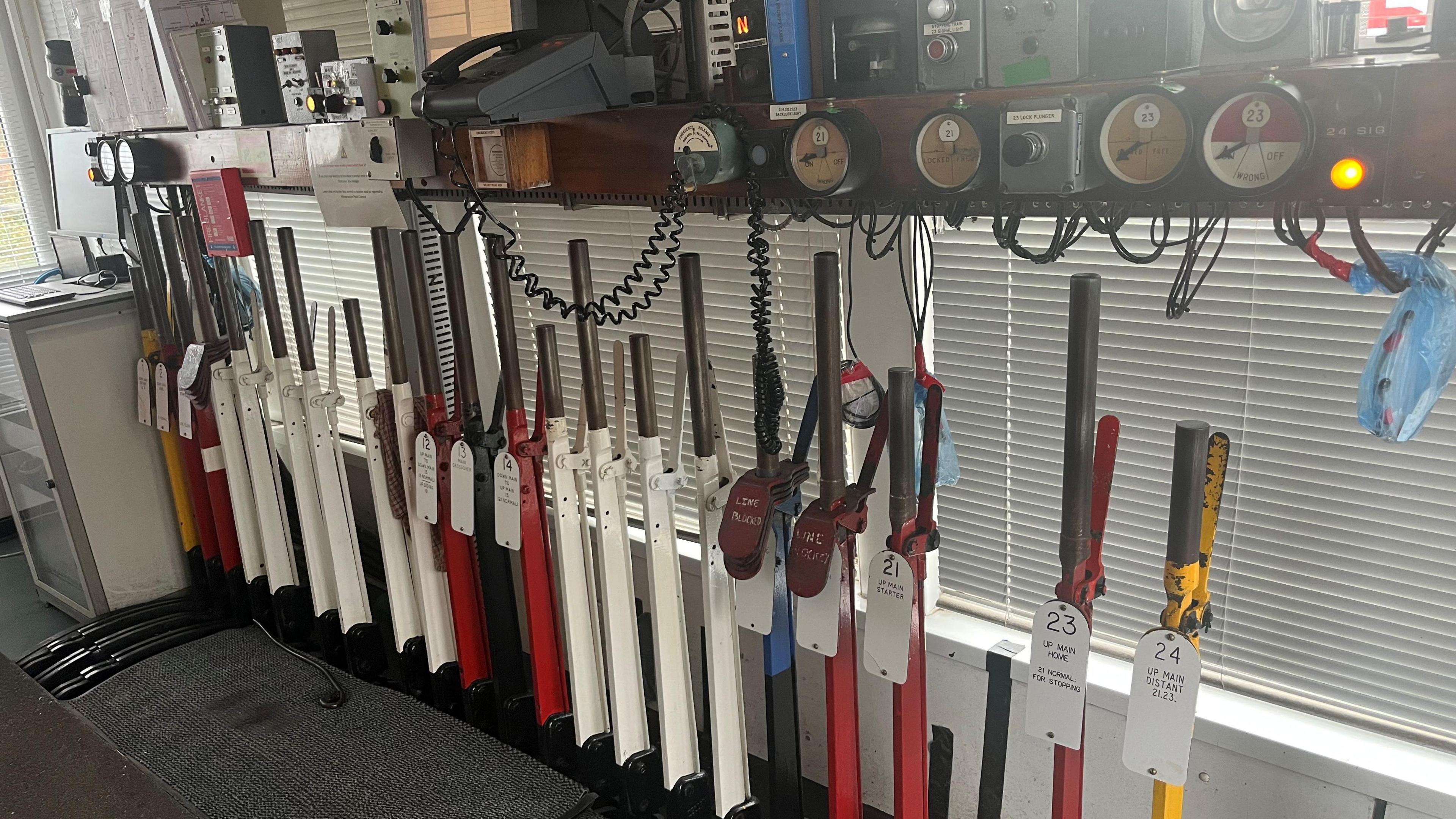 Inside a railway signal box where lots different coloured leavers, about 1m (3ft) high sit under a shelf with various electronic equipment on.