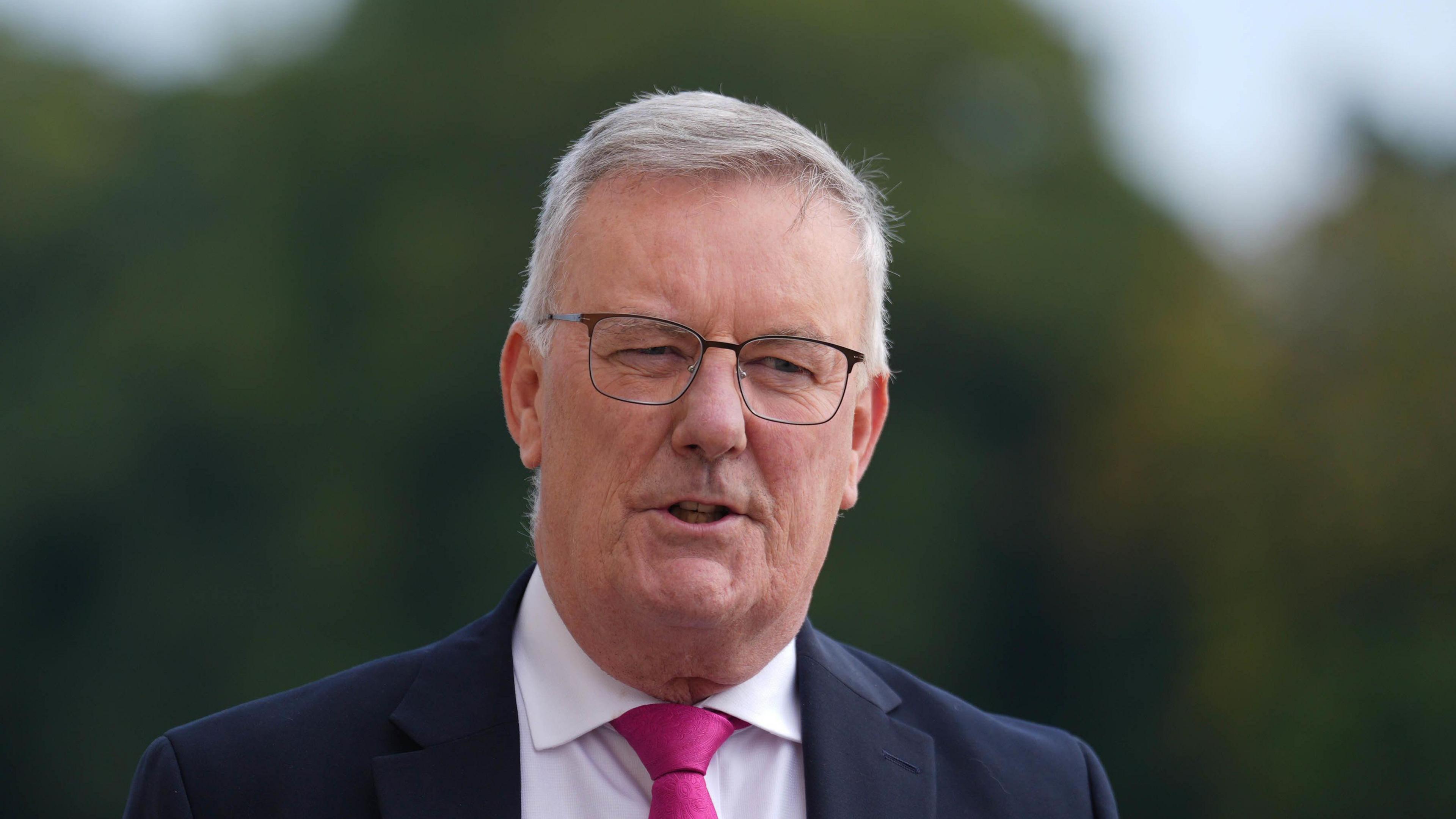 Mike Nesbitt wearing a dark coloured suit and a pink tie, with a white shirt. 