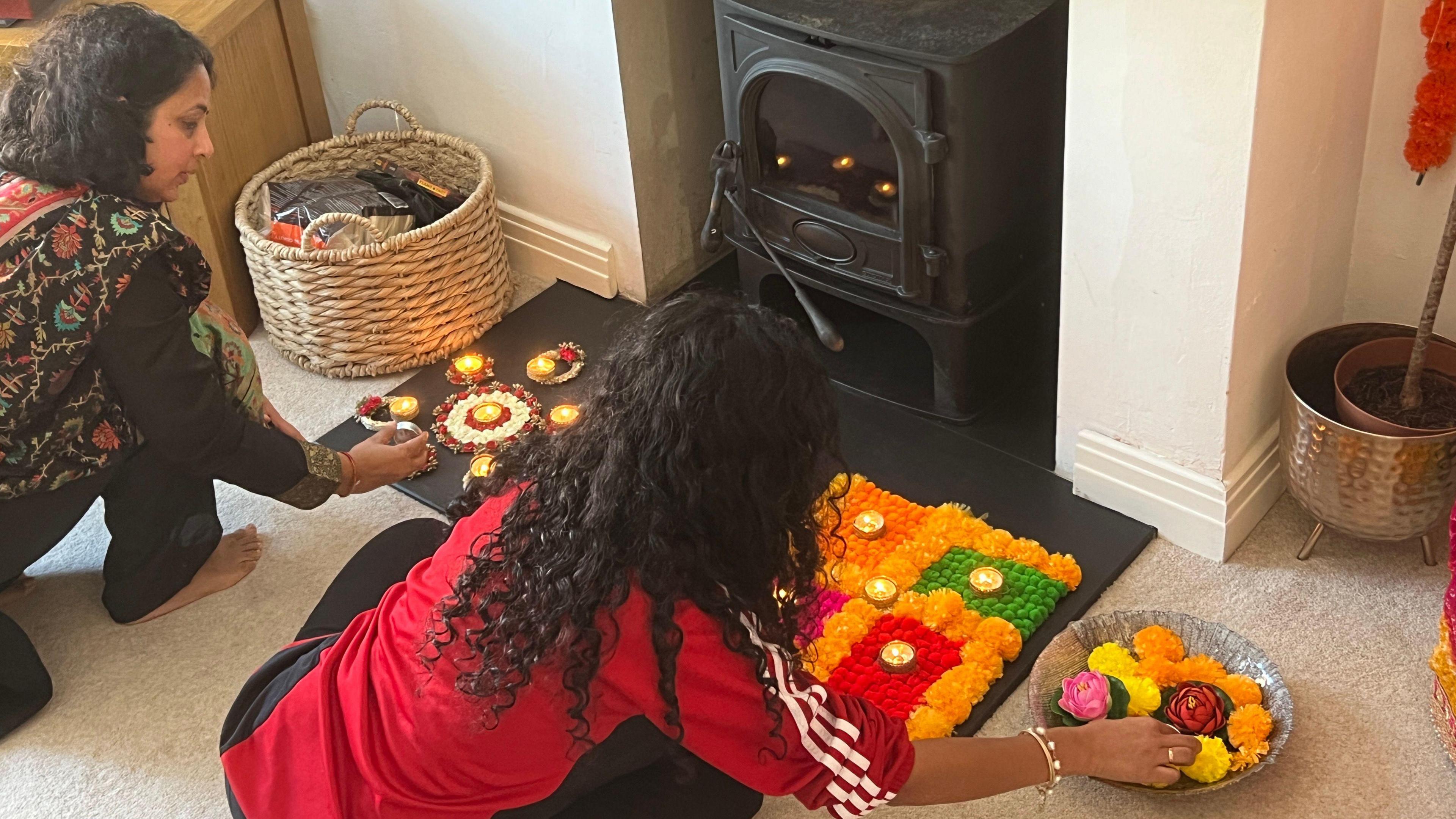 Two women decorating a fireplace with bright colours and small diyas