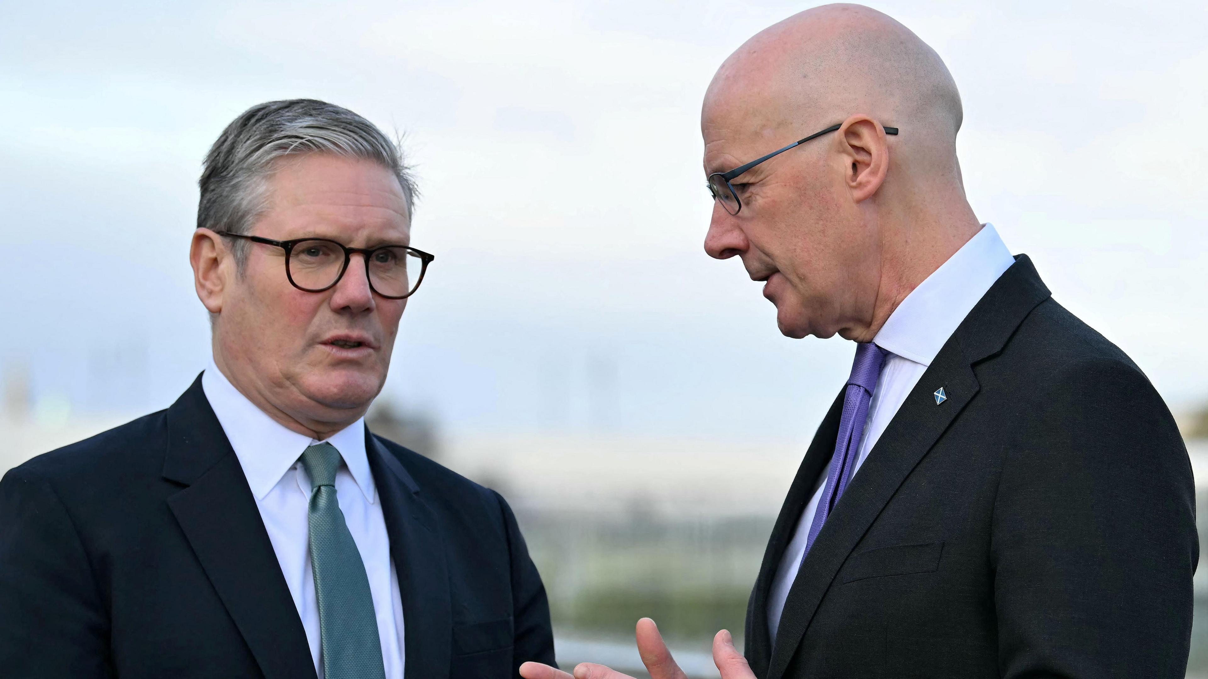 Sir Keir Starmer, who has grey hair and is wearing dark glasses with a dark suit, white shirt and grey tie is talking with John Swinney. Mr Swinney is a bald man with glasses who is also wearing a dark suit and white shirt but with a purple tie