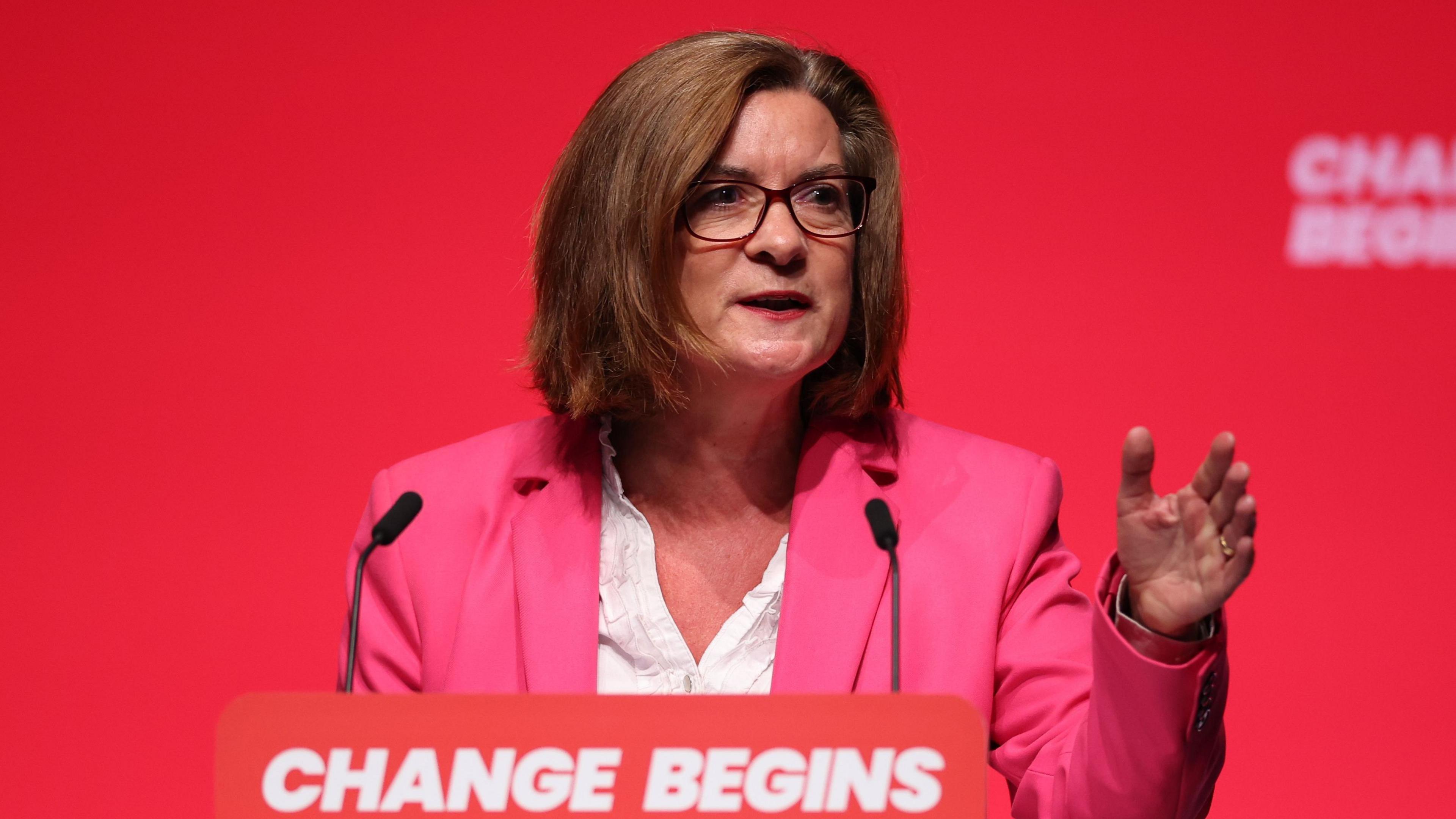 Eluned Morgan stood at a lectern at a Labour conference with the words "change begins" in capital letters written on a screen behind her and on the lectern.