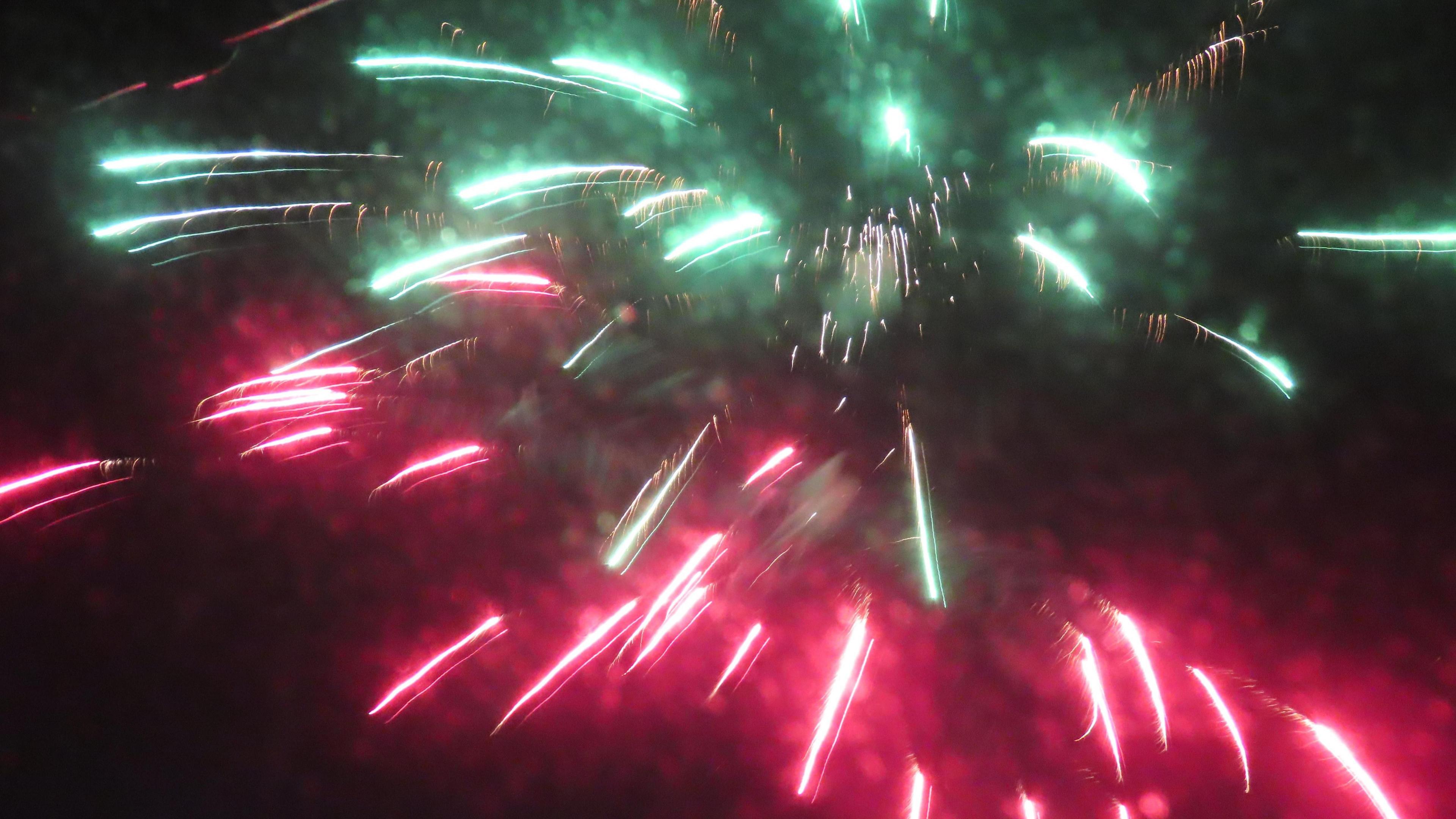 Bursts of red and green light up from firework bursts against a black sky.