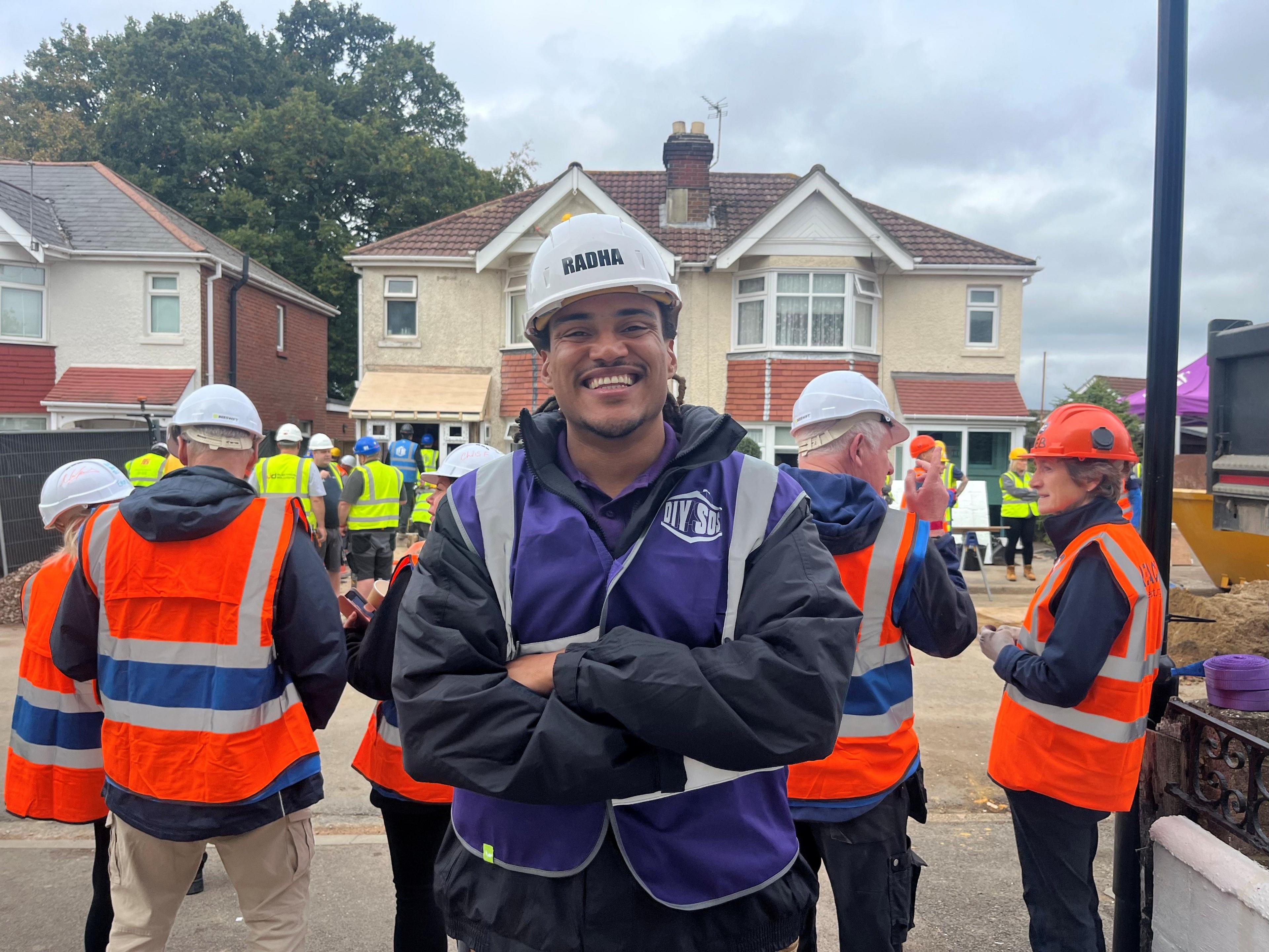 Radha Siyver smiles at the camera wearing a purple florescent vest and a white hard hat. 