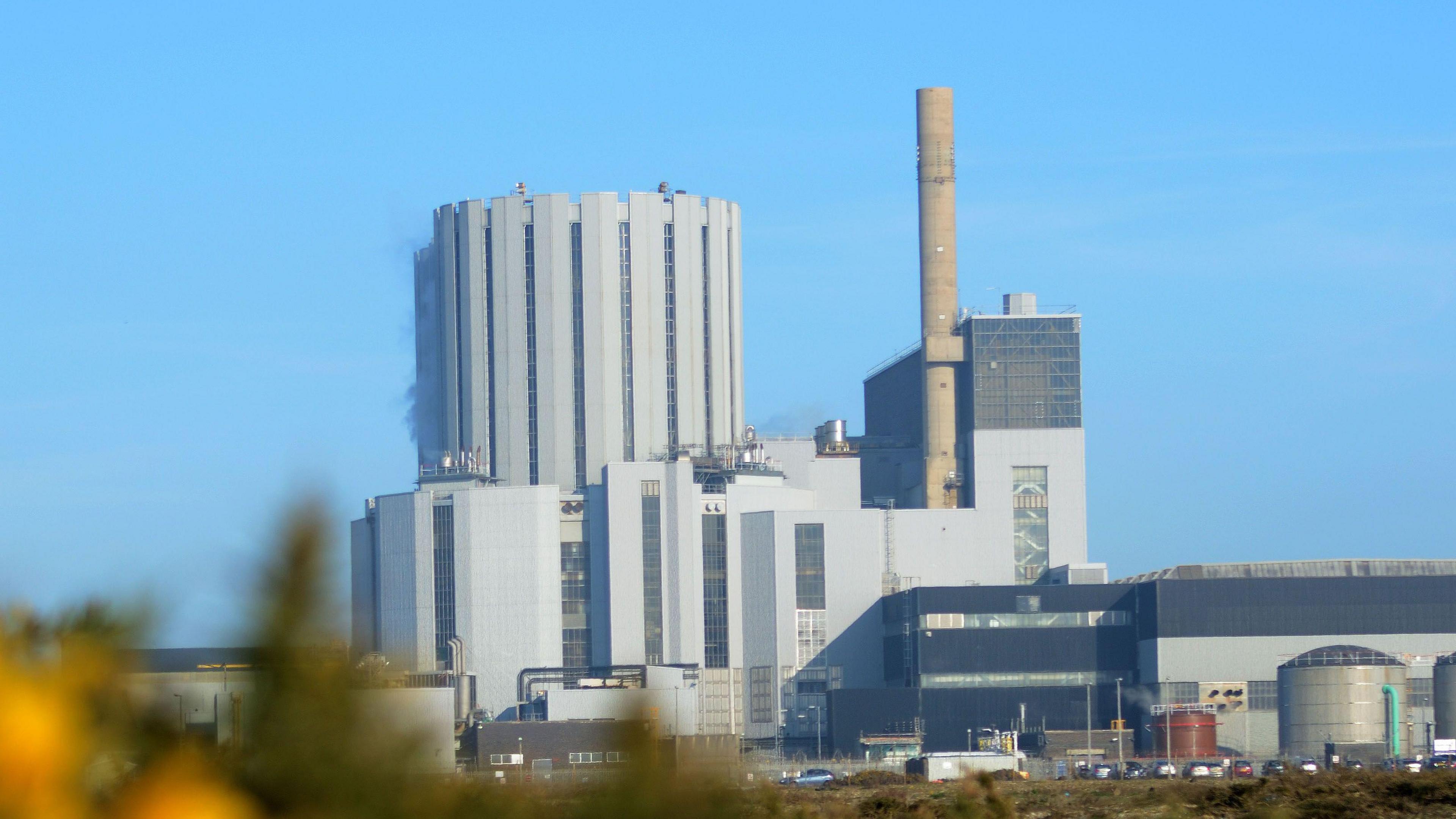 A view of the outside of Dungeness B nuclear power station, showing cooling towers and grey buildings.