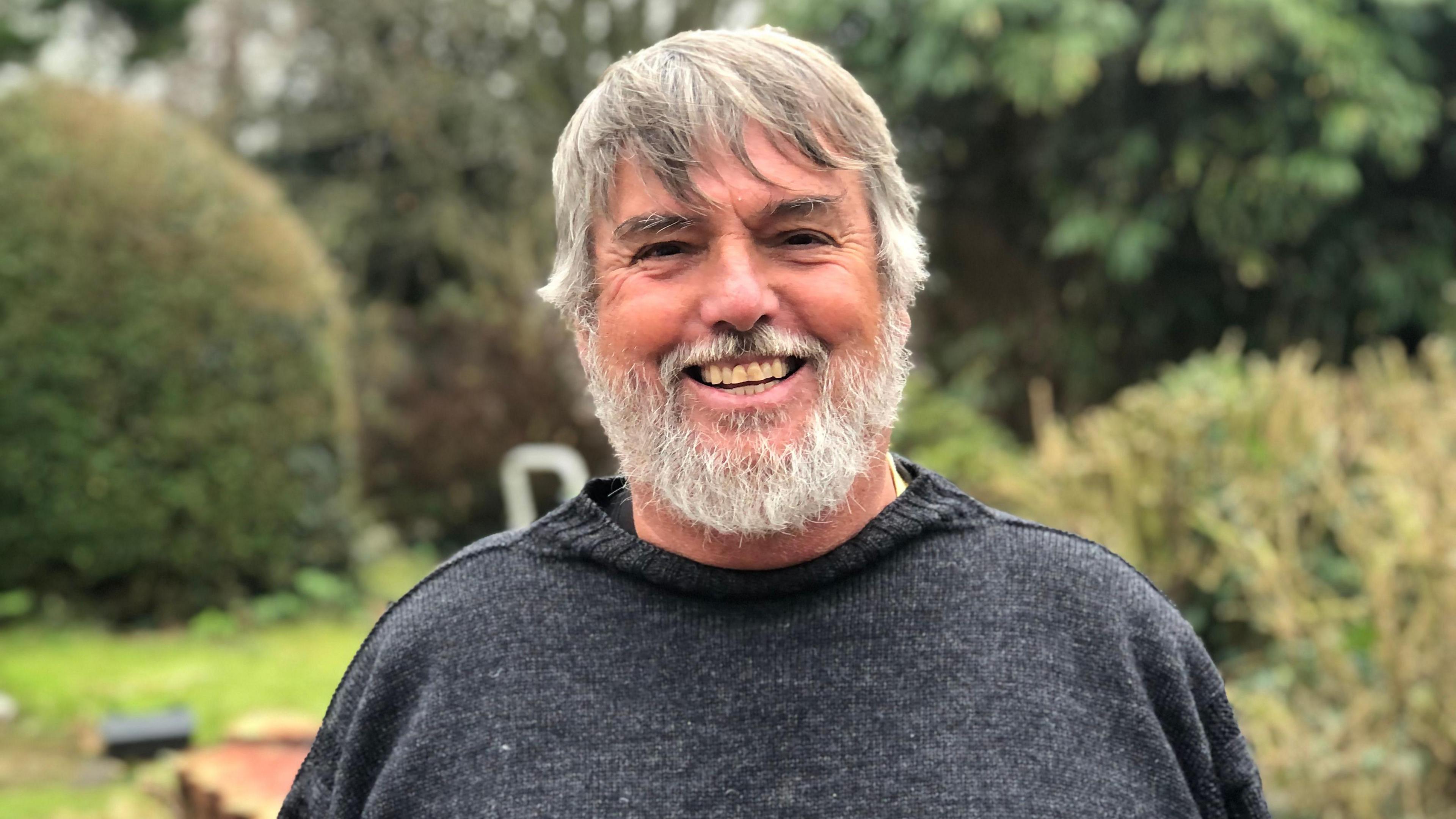 Man in a Guernsey jumper with grey hair and beard smiling at the camera