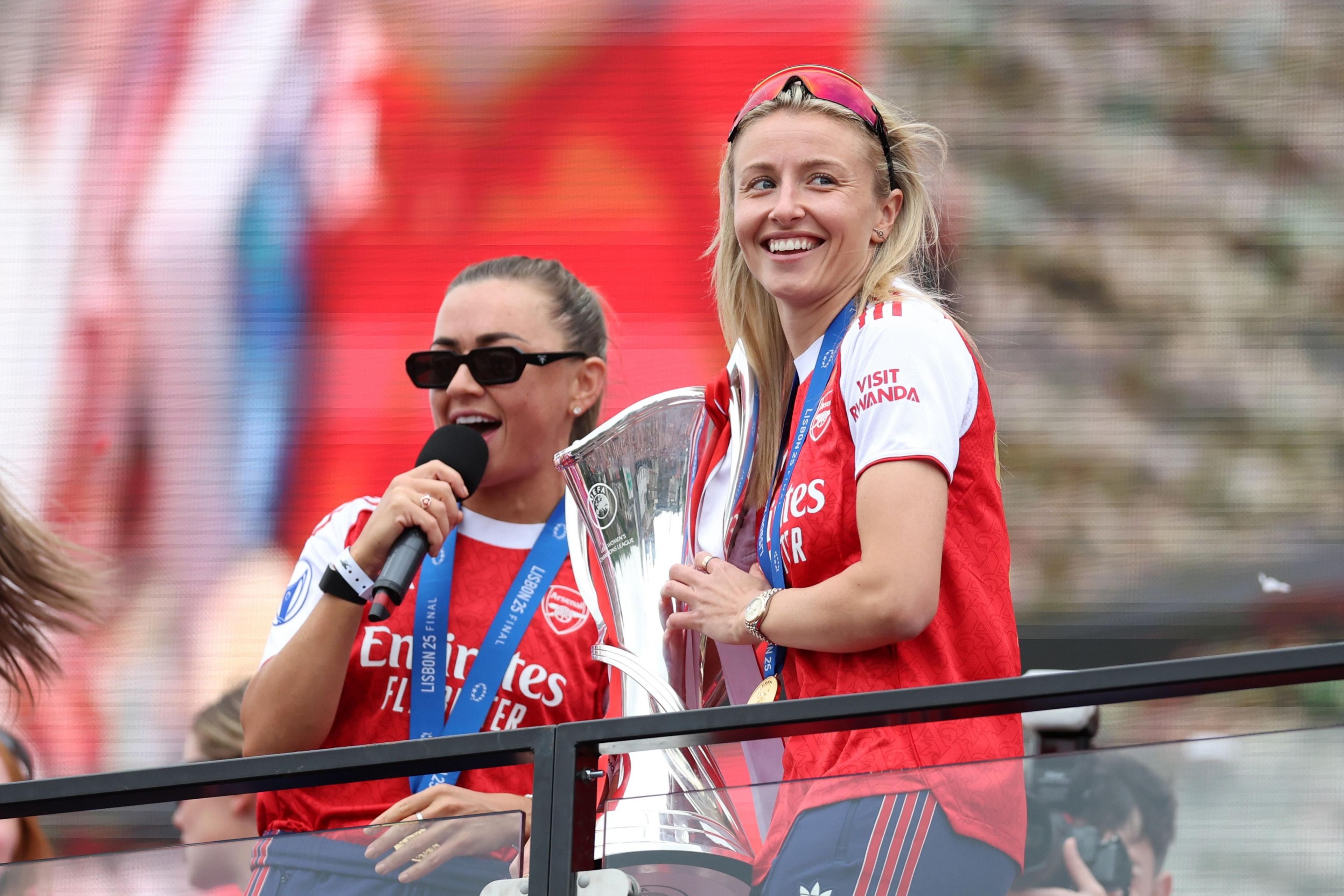 Katie McCabe sings on the microphone as Leah Williamson holds the trophy