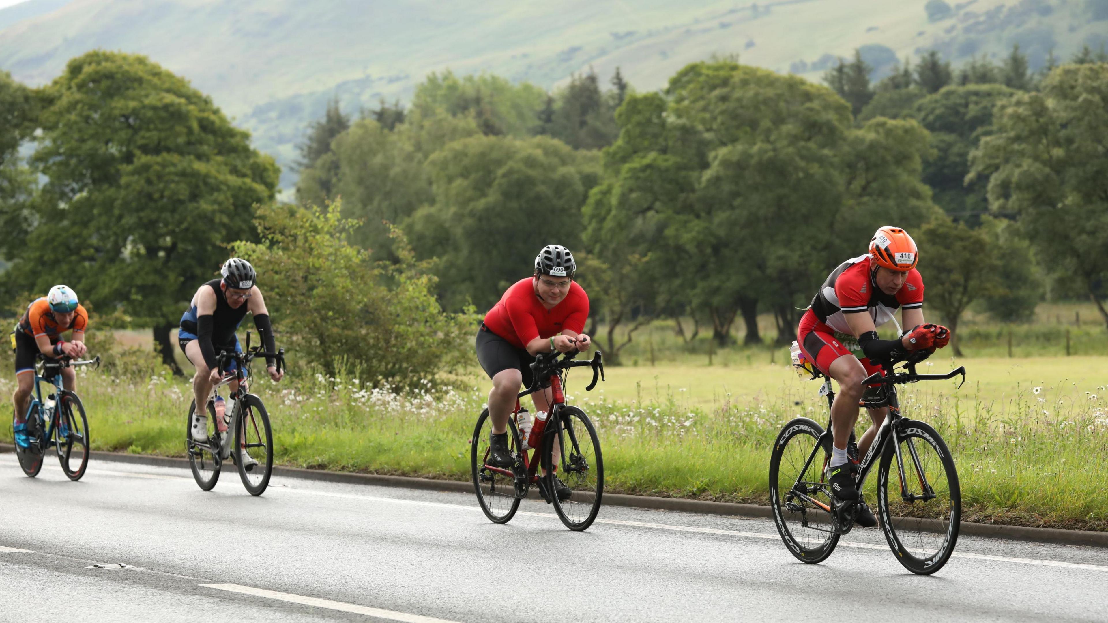 Four men on bikes with a backdrop of trees and hills. 