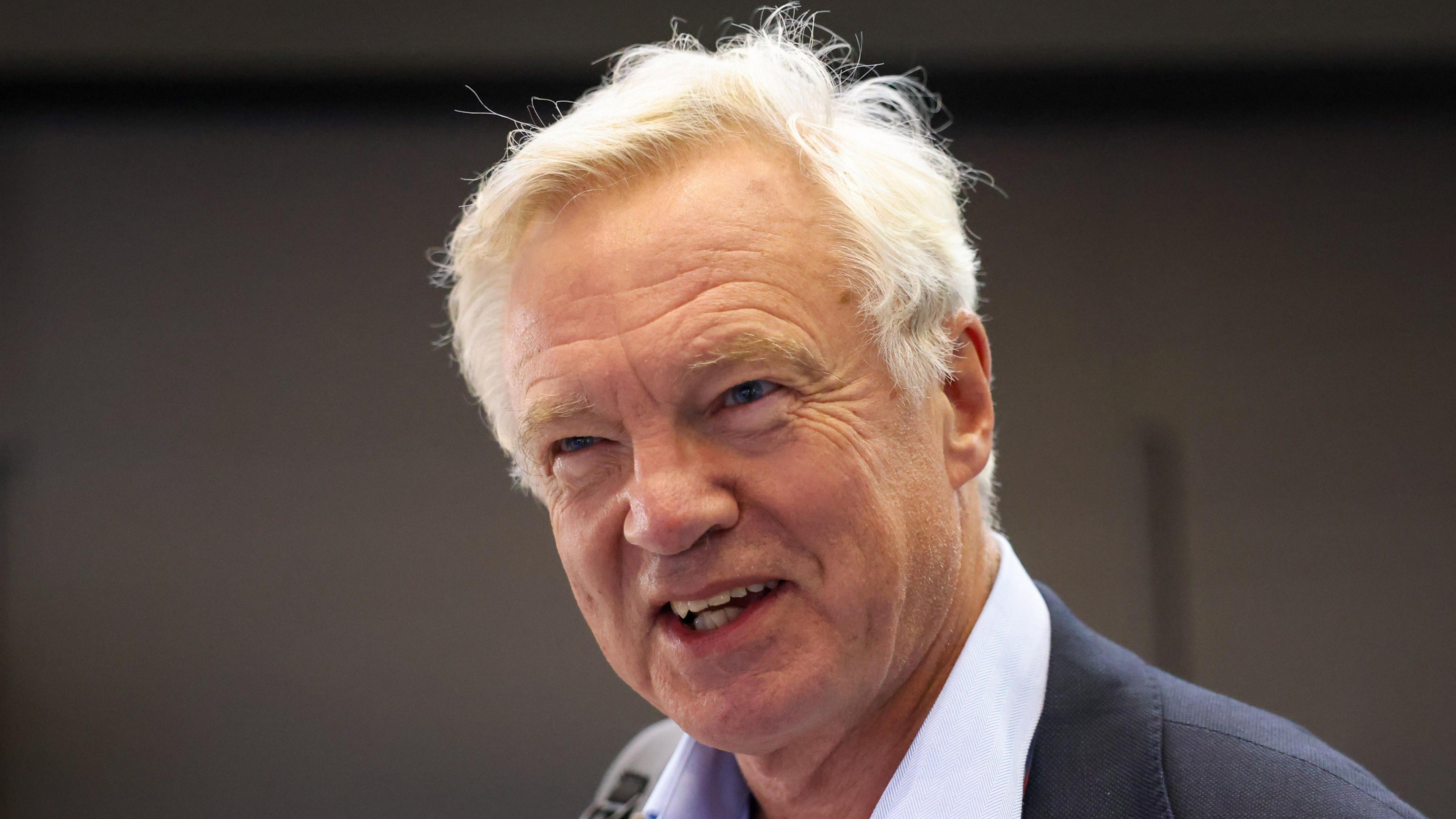 David Davis, with white hair blowing about, smiles at the camera in an open necked shirt
