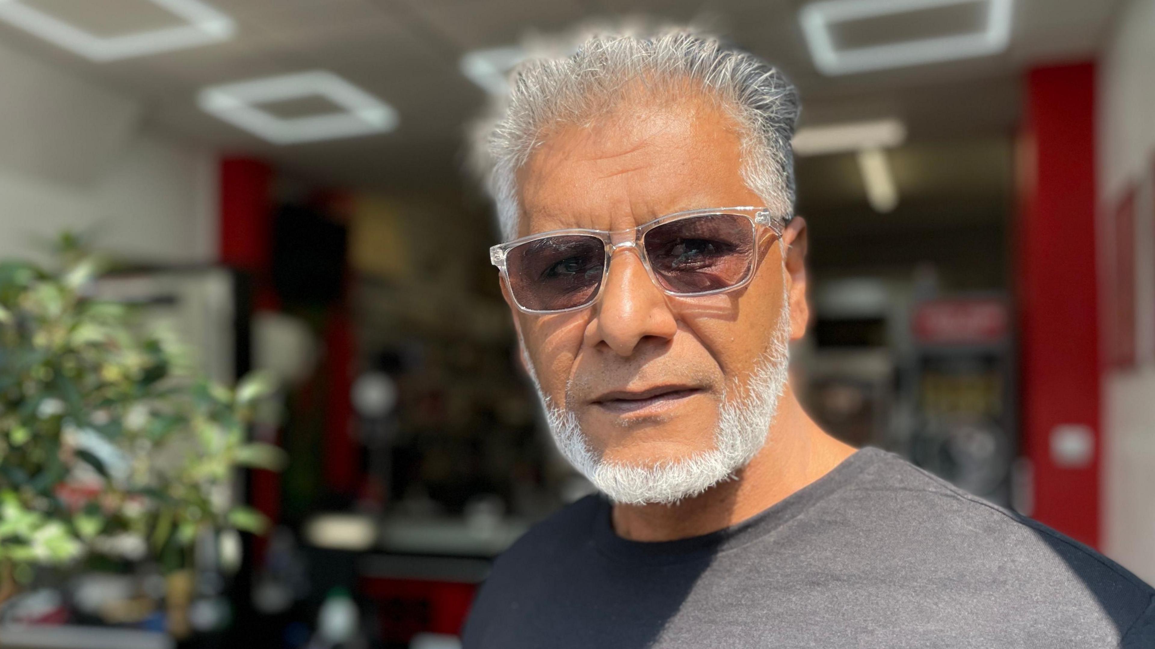 Jamil Ellahi in a grey t-shirt and sunglasses with a white beared