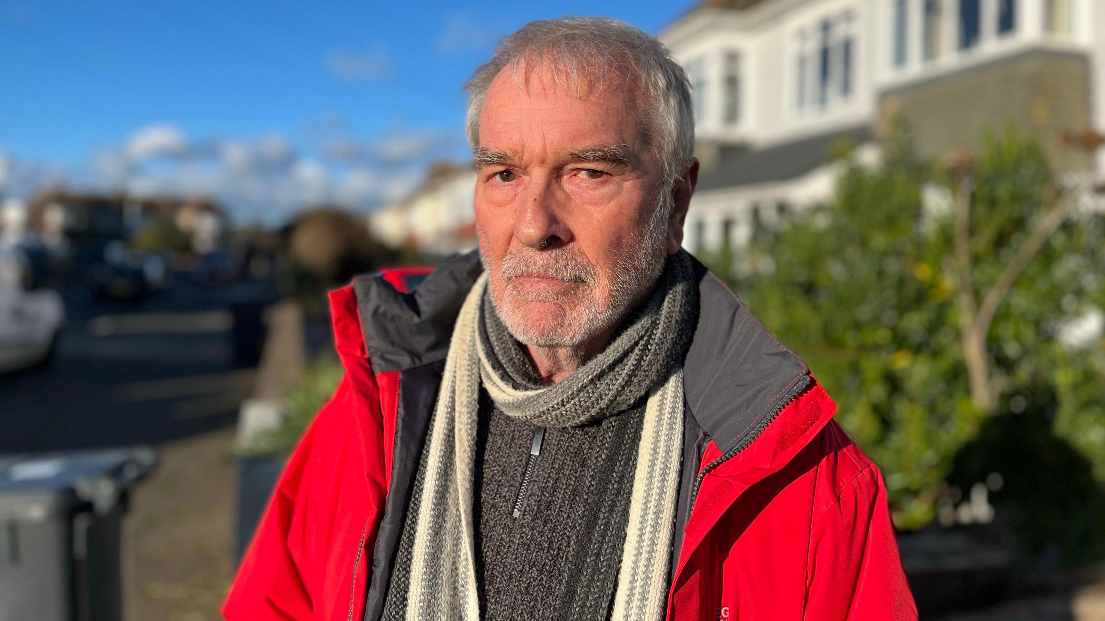 Mike Whiting, wearing a red windcheater, grey sweater and white scarf.