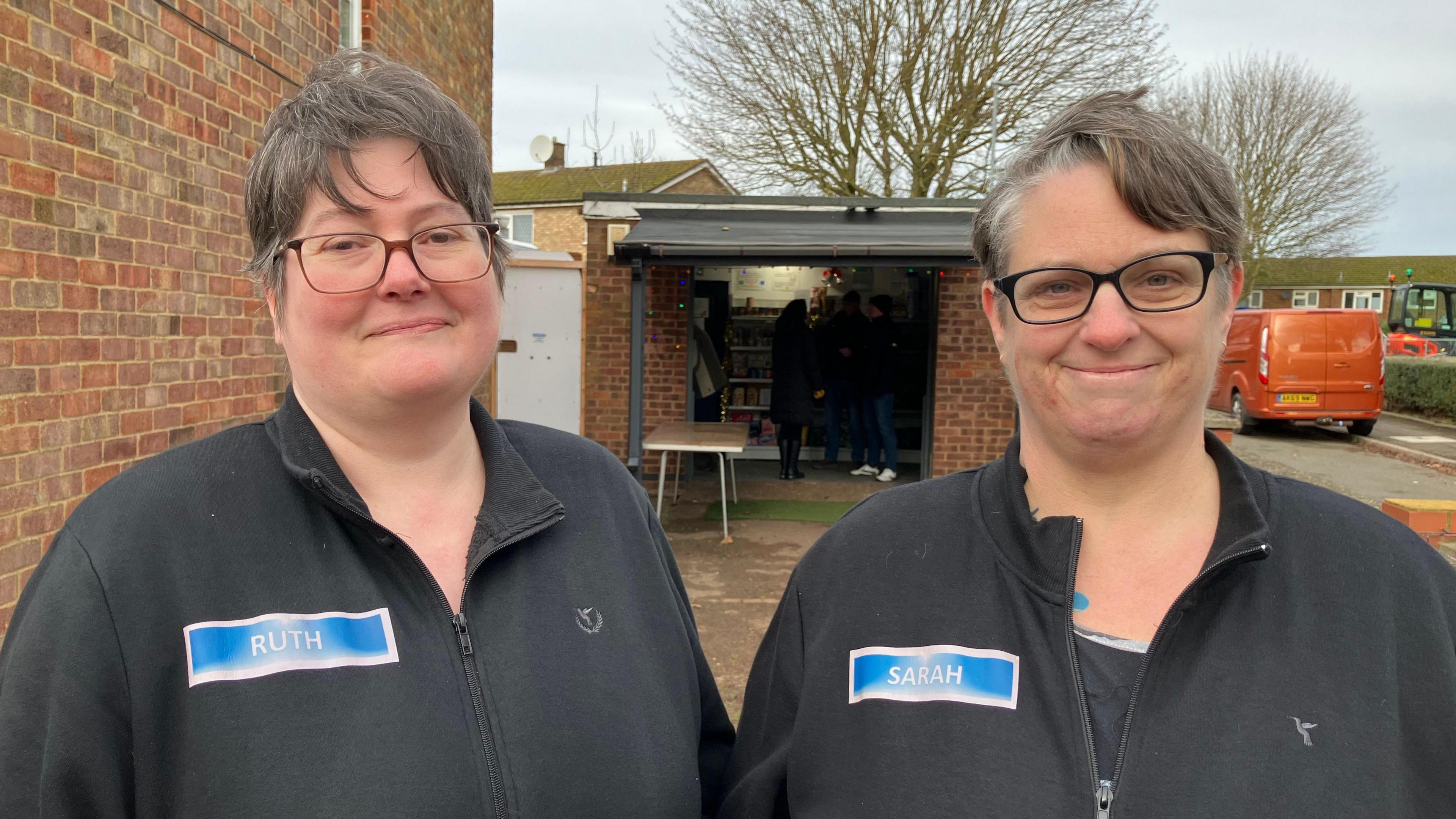 Two women with glasses in black jackets stand outside