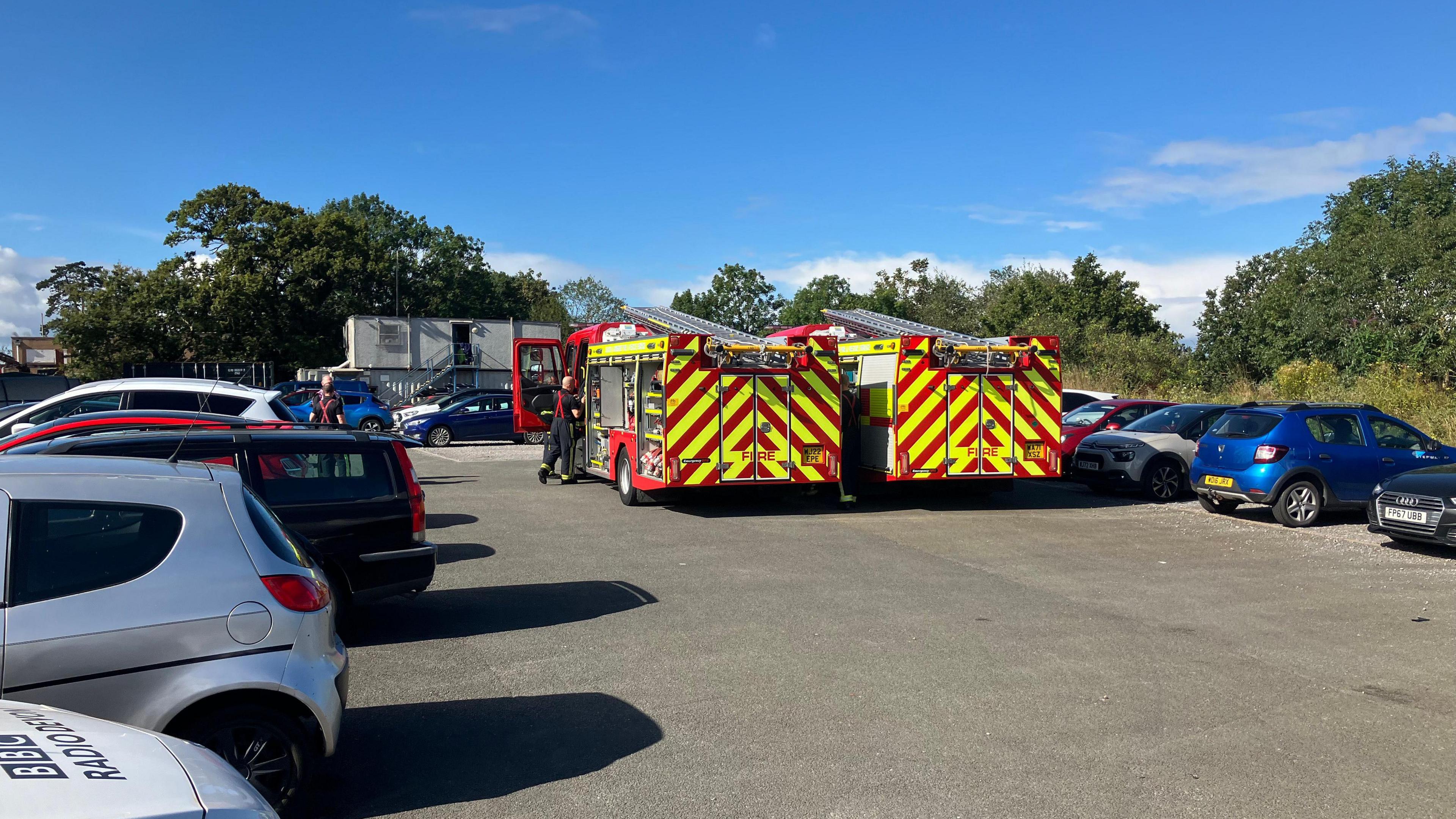 Two fire engines in a car park while dealing with an incident in Exmouth. One firefighter is getting into one of the vehicles.