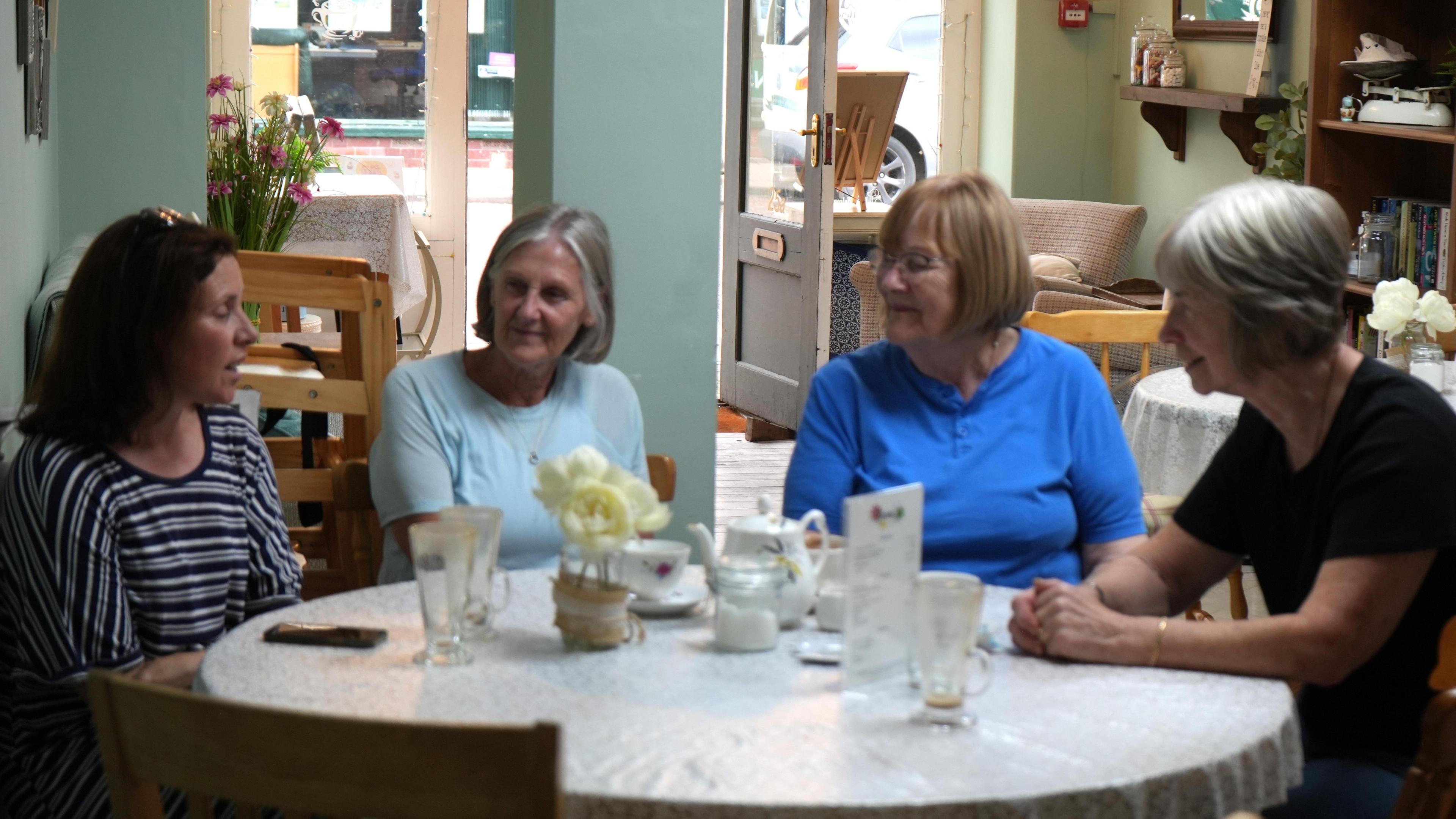 Four women sit around a table, chatting in a cafe