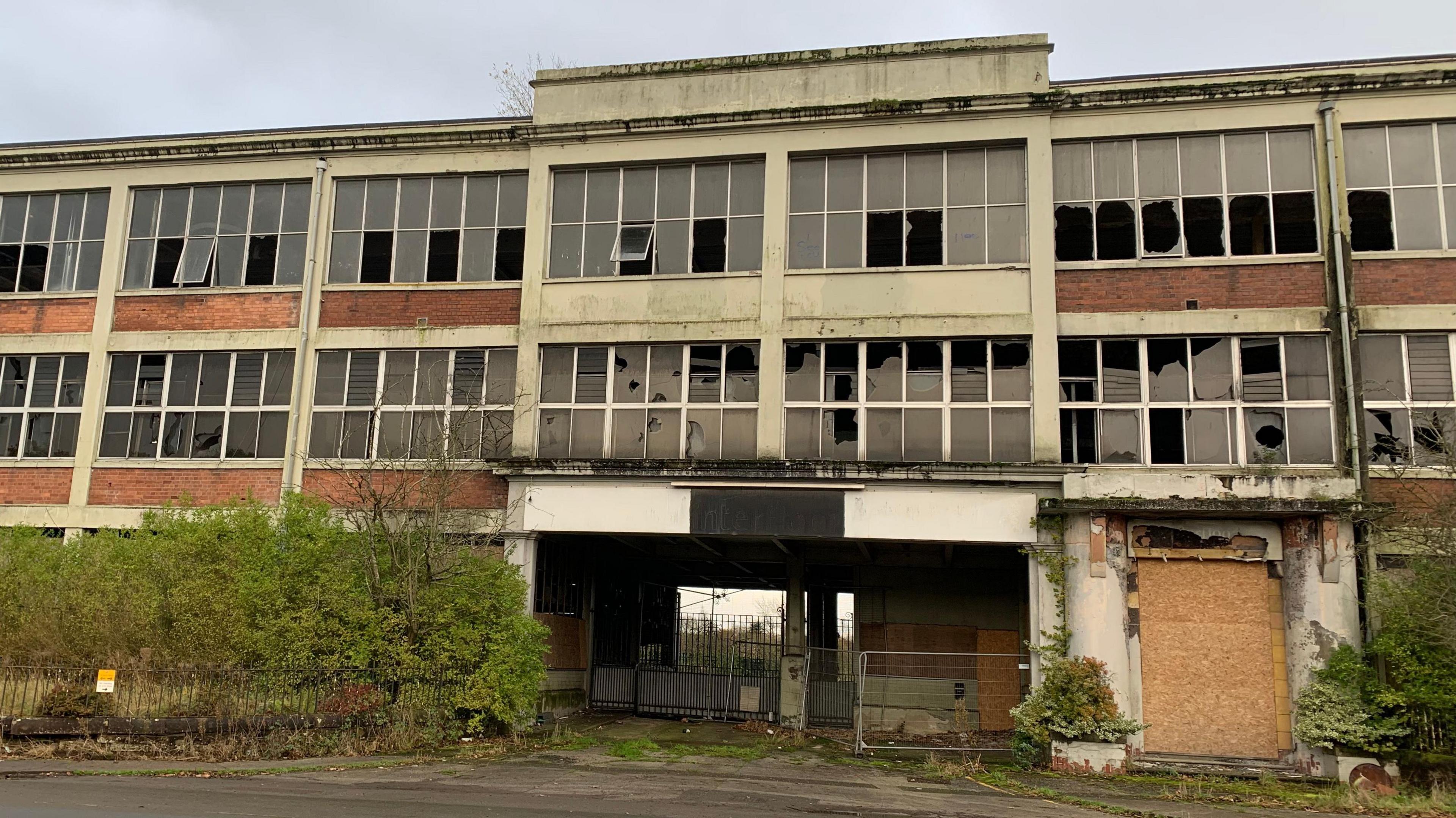 A derelict building frontage with smashed windows and a boarded up doorway