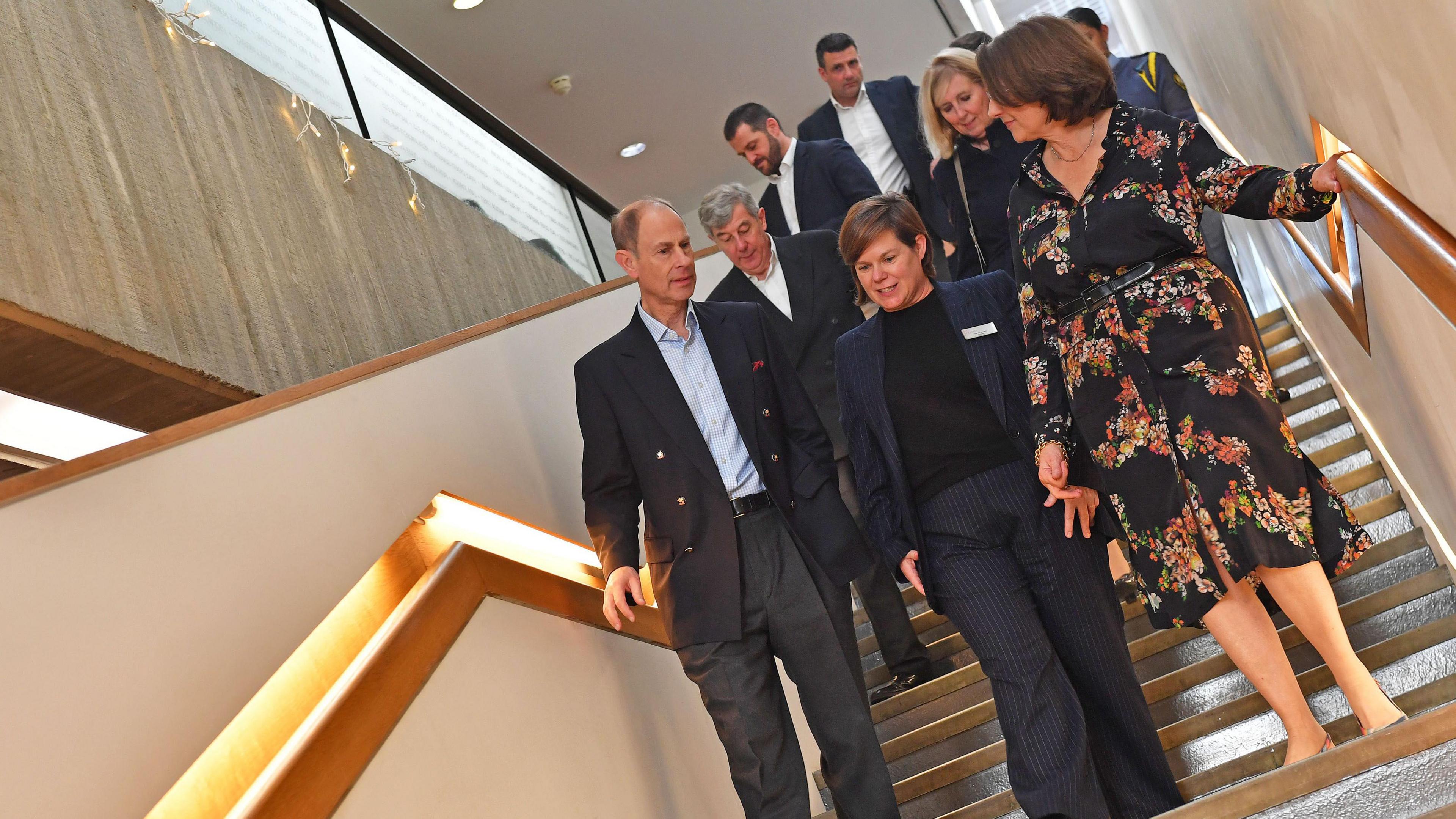 Seven people walking down a flight of stairs. One of them is the Duke of Edinburgh