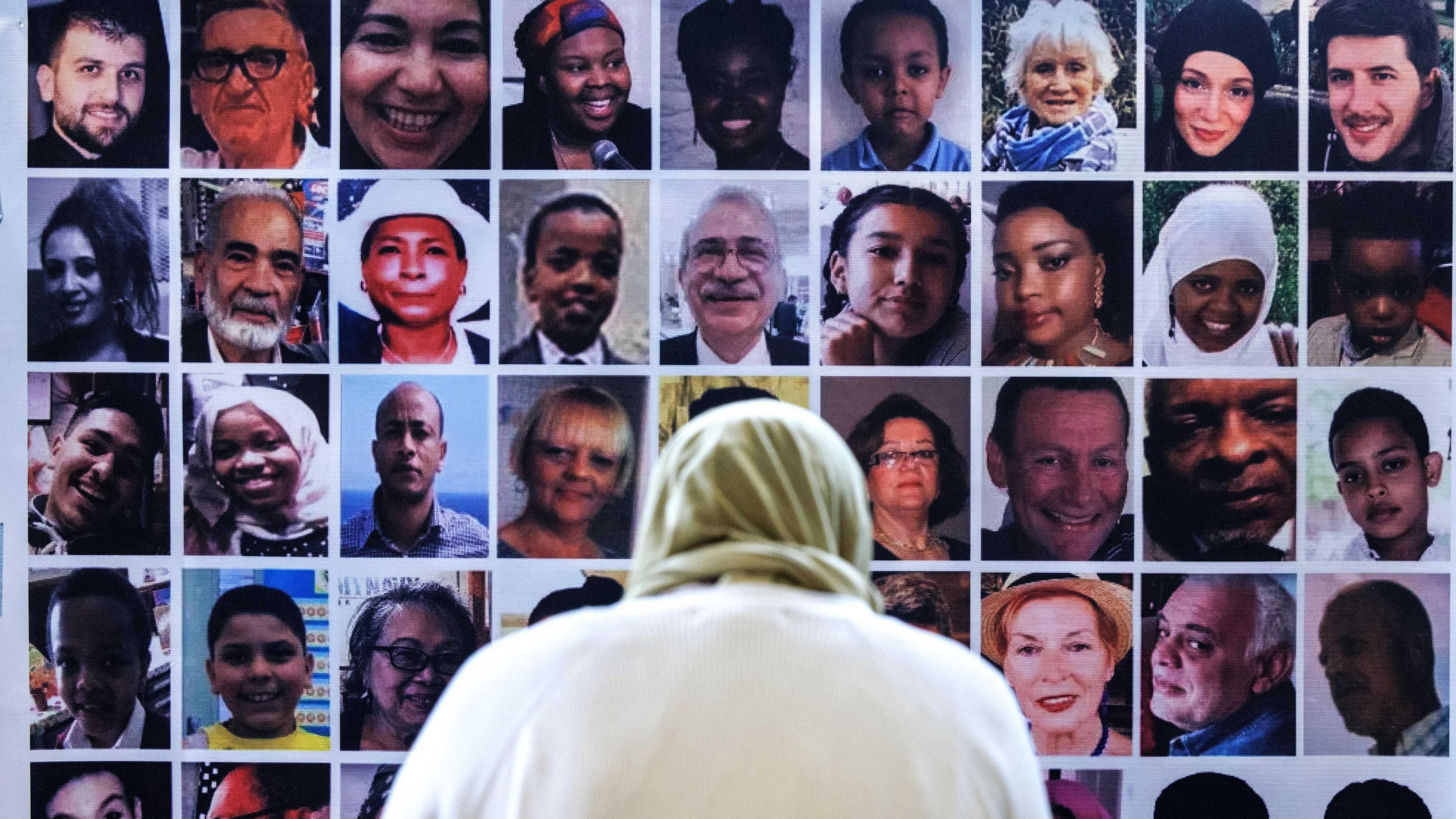 An woman, wearing a light green headscarf, stands with her back to the camera looking at a montage of photos of the victims of the Grenfell fire. 