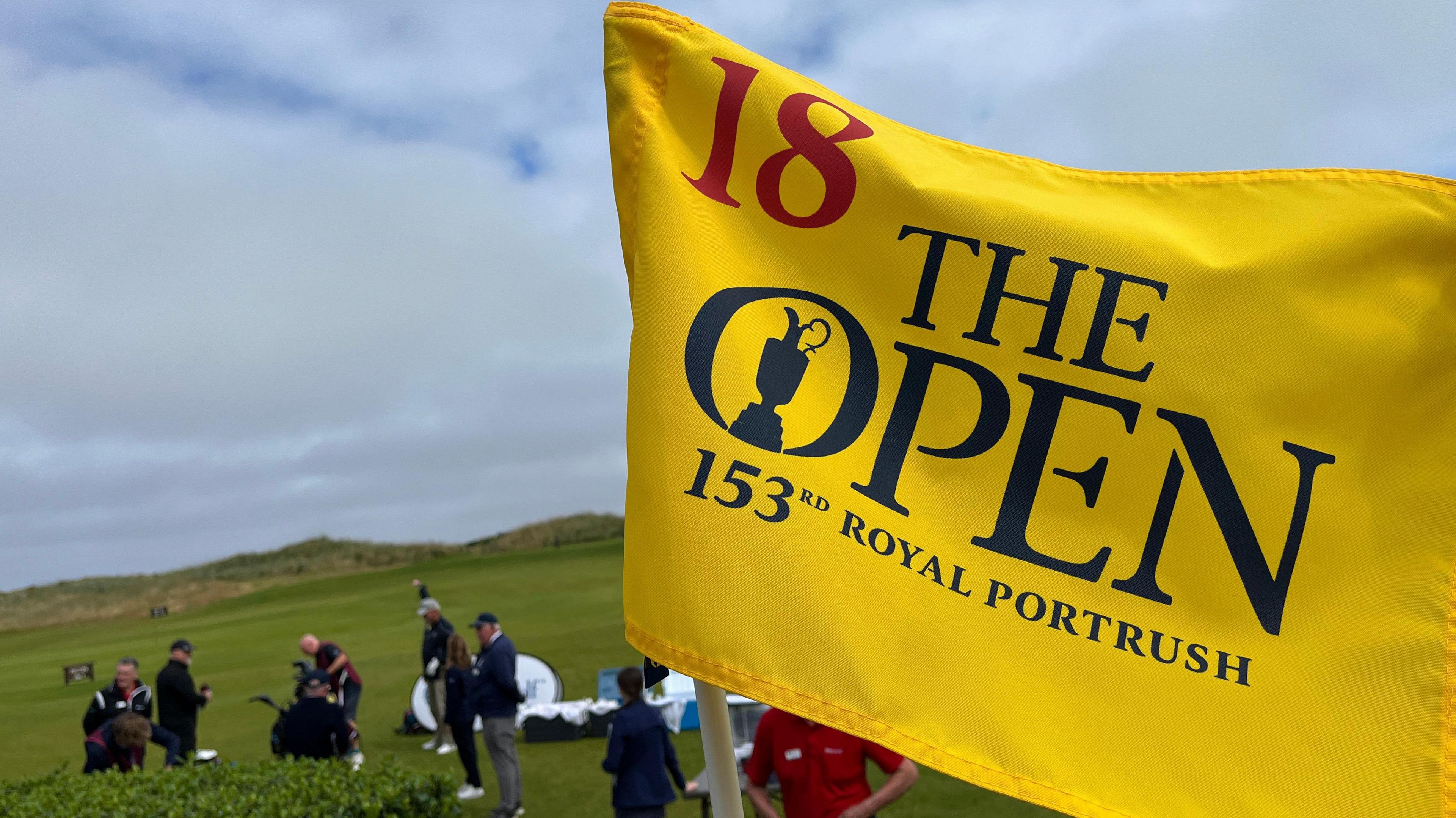 A yellow golf flag on the Royal Portrush course with 'The Open 153rd Royal Portrush' written in navy letters