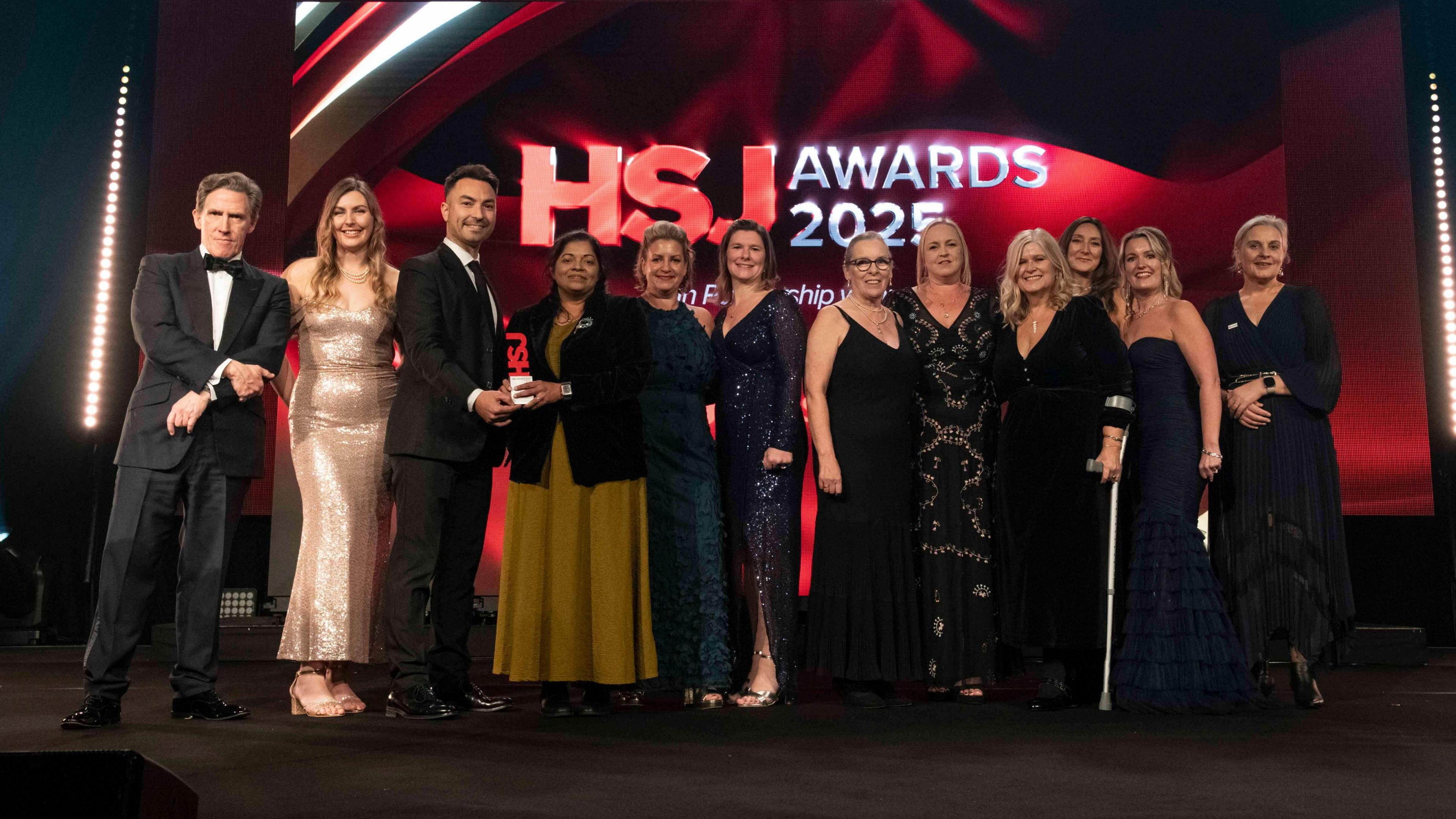 A group of men and women stood on stage accepting an award, dressed in black tie