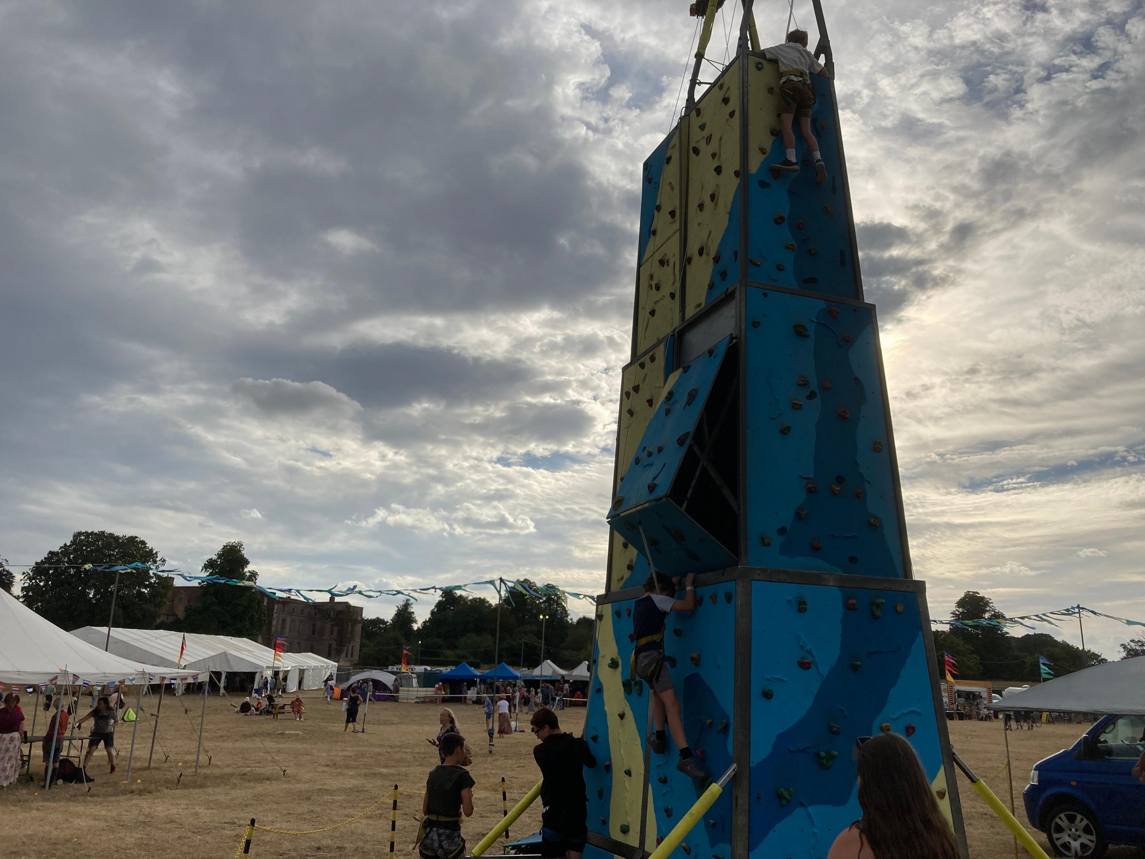 A wooden climbing wall/tower painted blue and yellow in the middle of the FolkEast festival field.