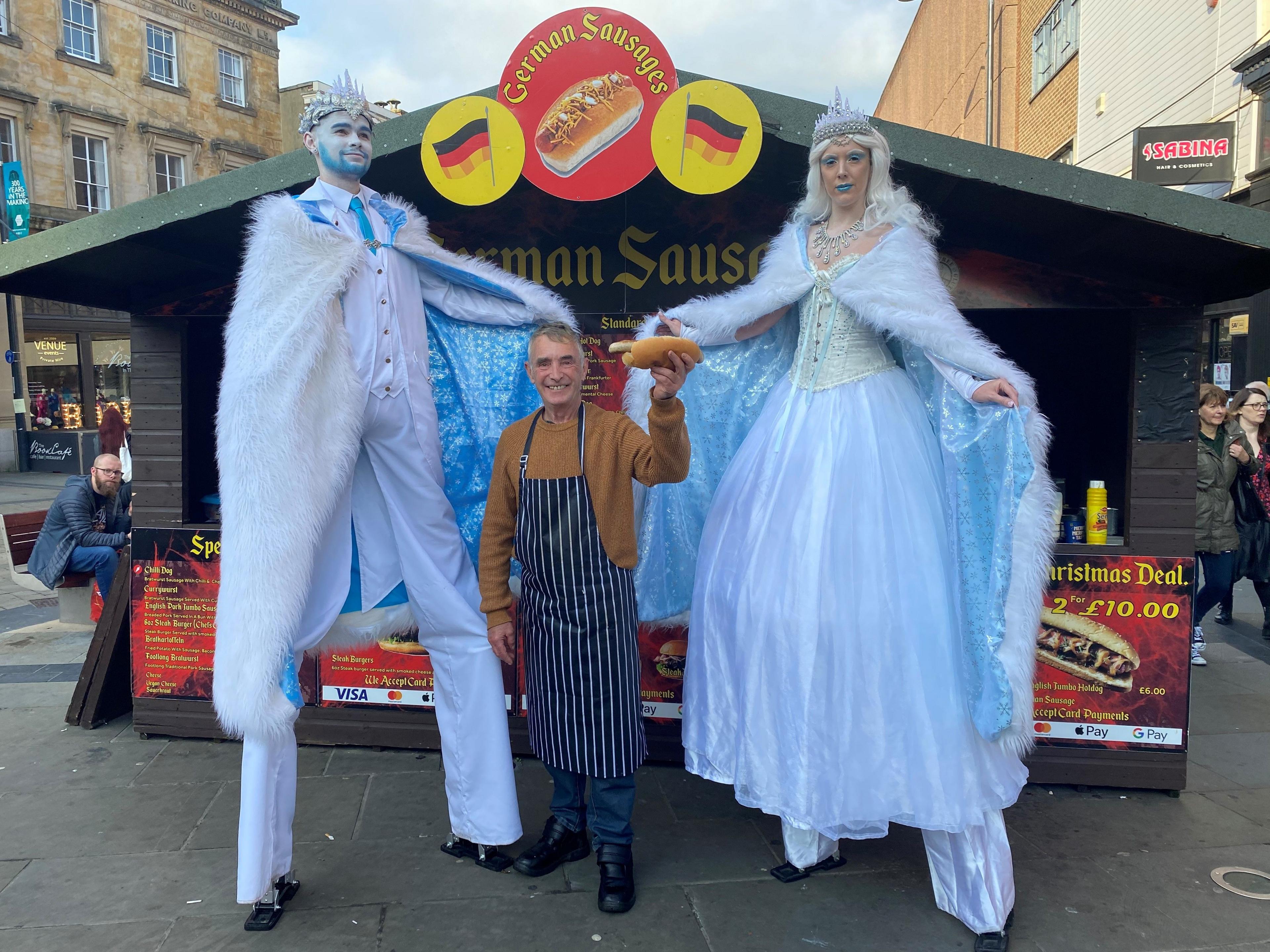 Charlie Pearson and two street entertainers on stilts stand outside his German sausage stall in happier times