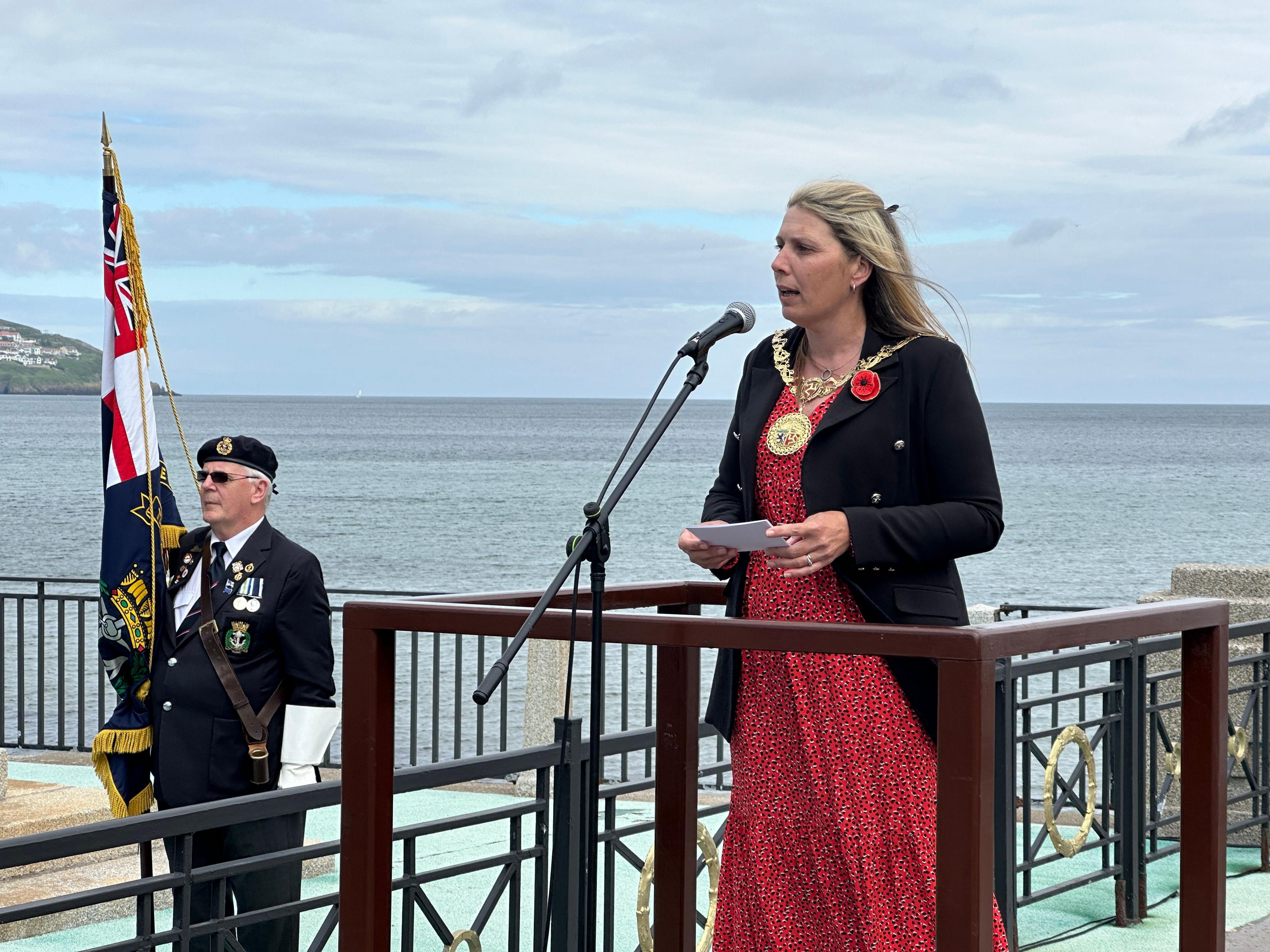 Natalie Byron-Teare in a red dress and black blazer is stood on a stage