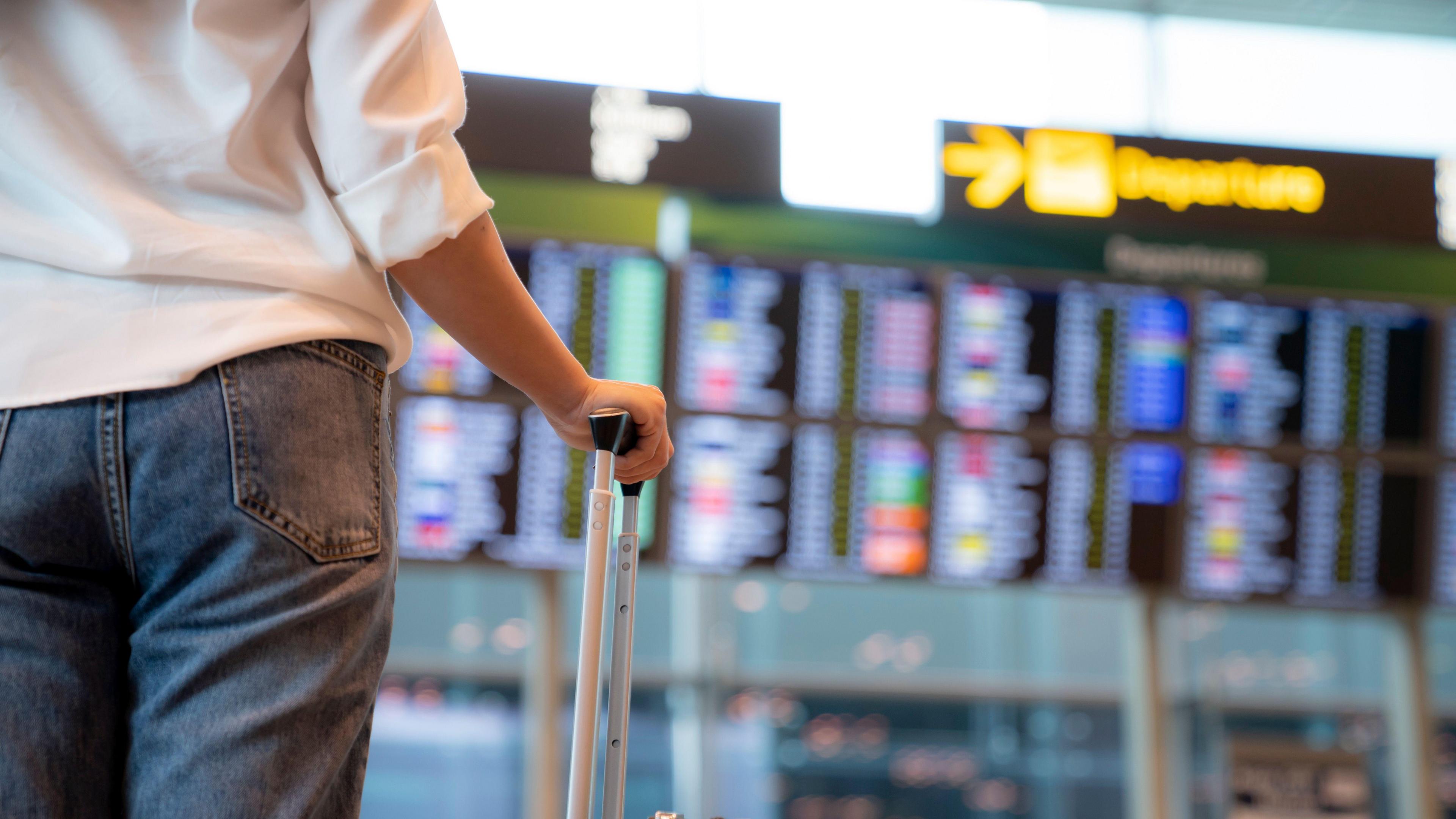 A woman looking at airport departure boards. The boards can be seen in the background, although they are out of focus. 