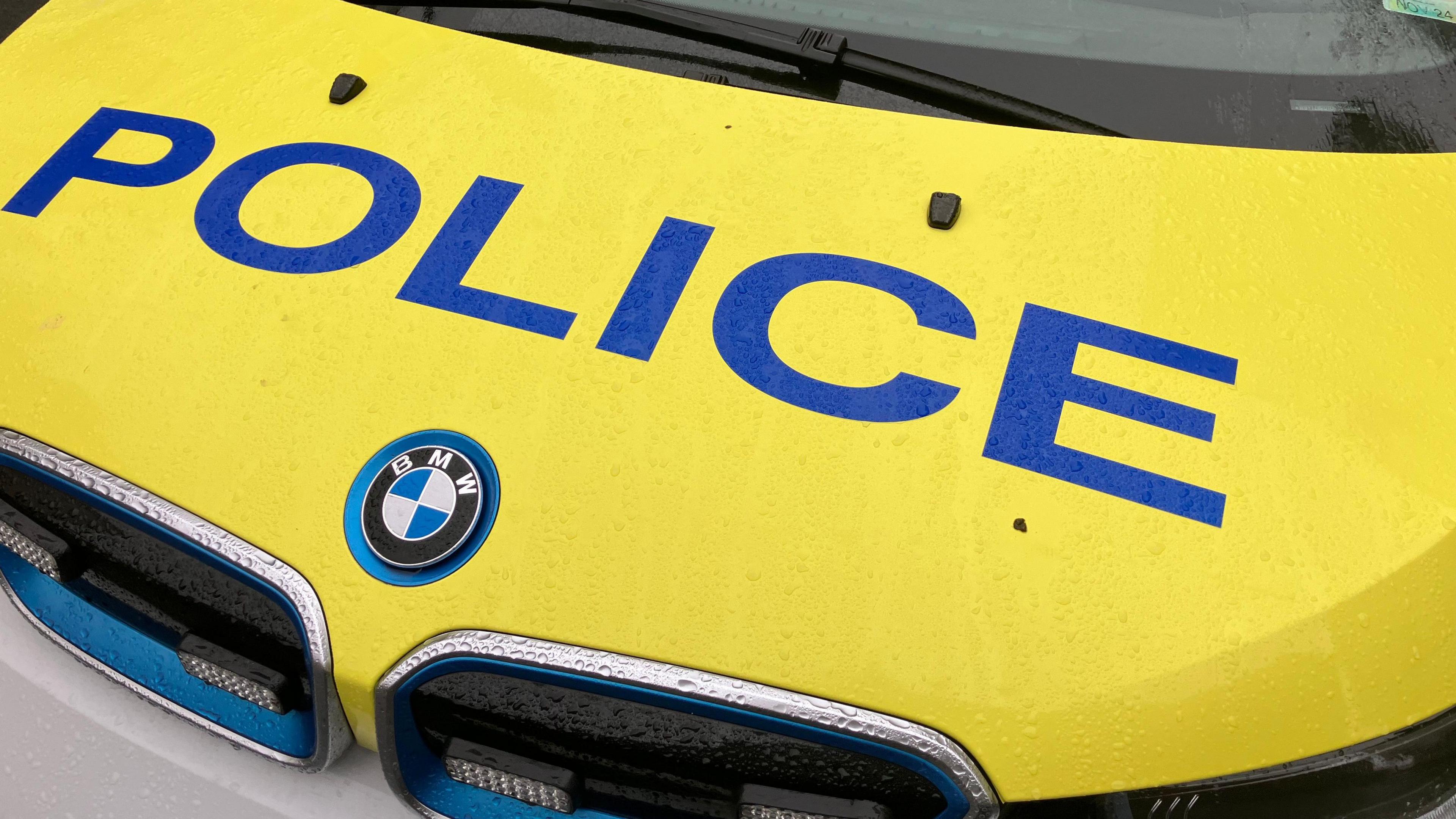 The bonnet of a Guernsey Police car. It is yellow with the word Police written in a blue, and a BMW badge.